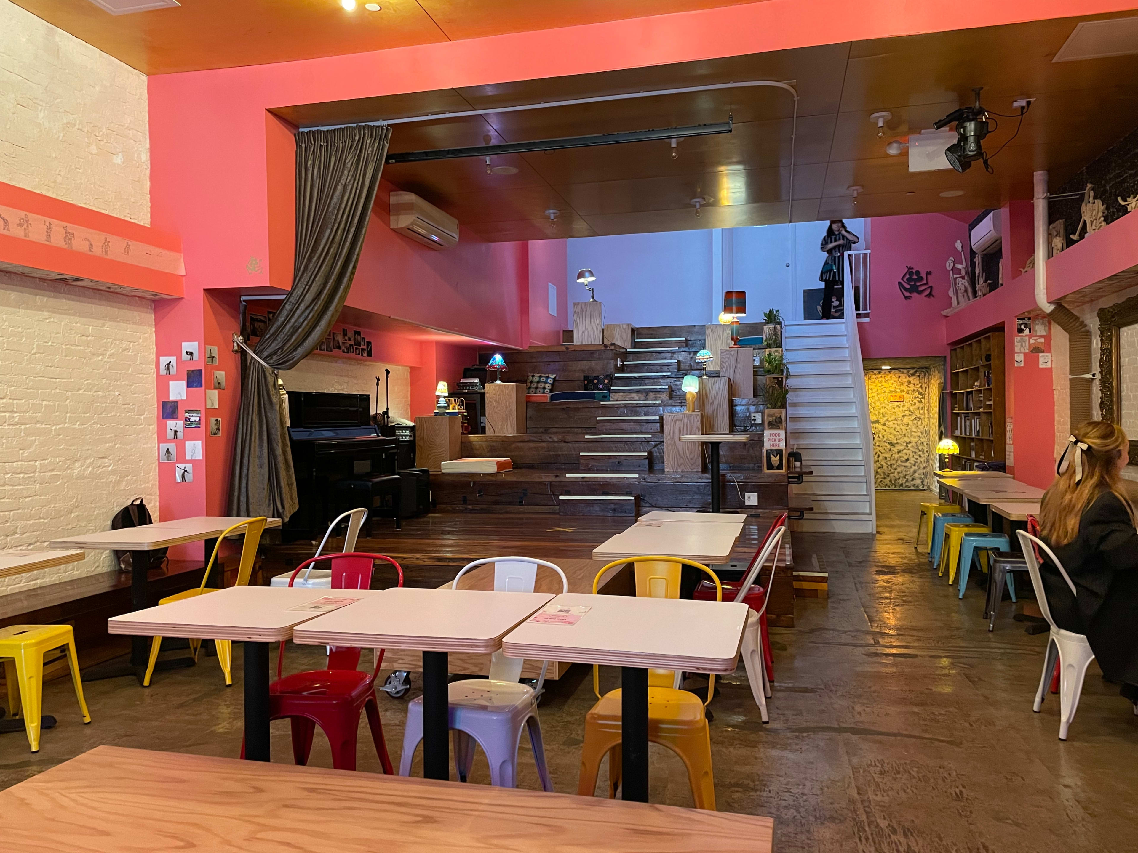 A vibrant café interior with wooden steps leading to an upper level, surrounded by colorful tables and chairs.