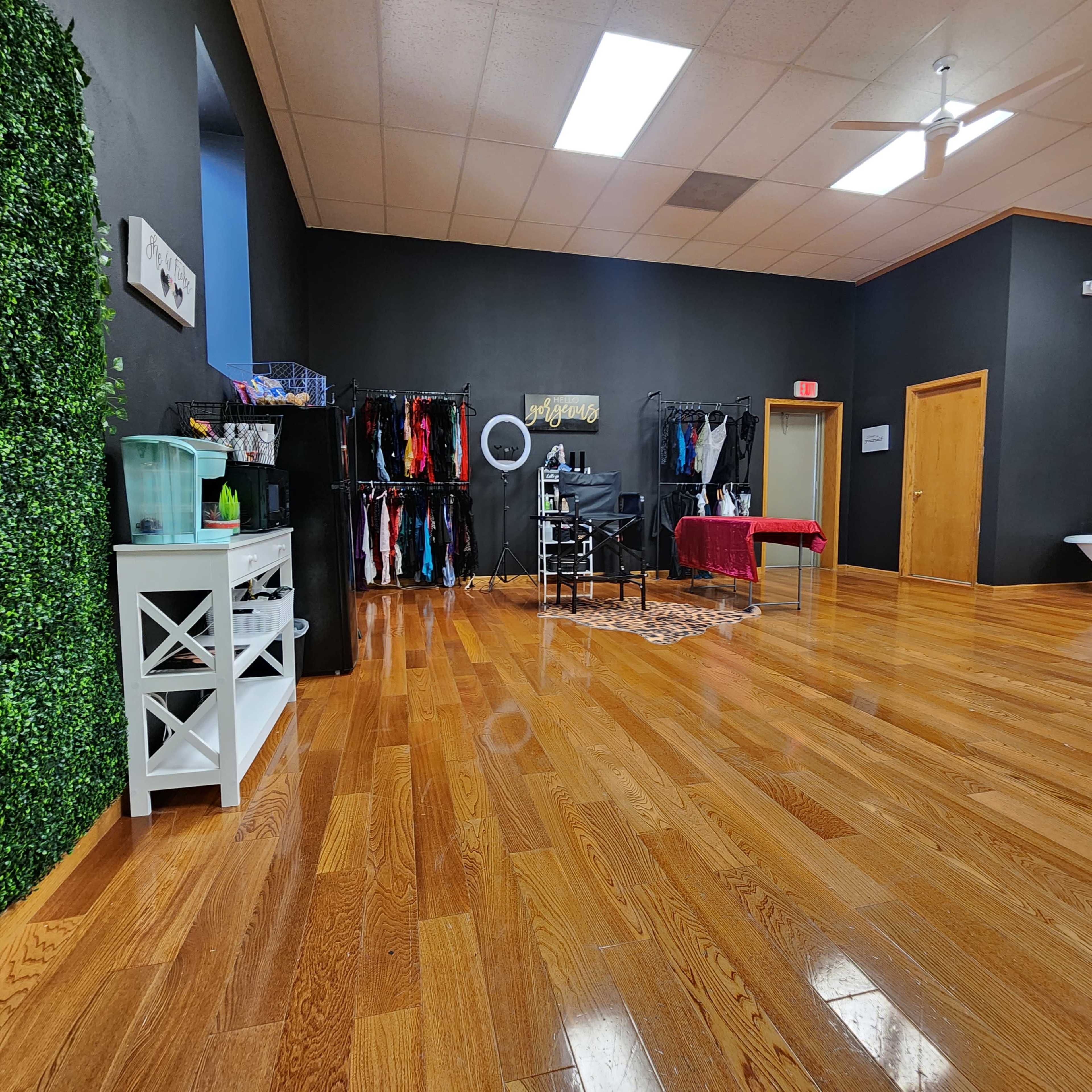 A spacious room with glossy wooden floors, black walls, a clothing rack filled with various garments, and a white shelving unit with a water dispenser.