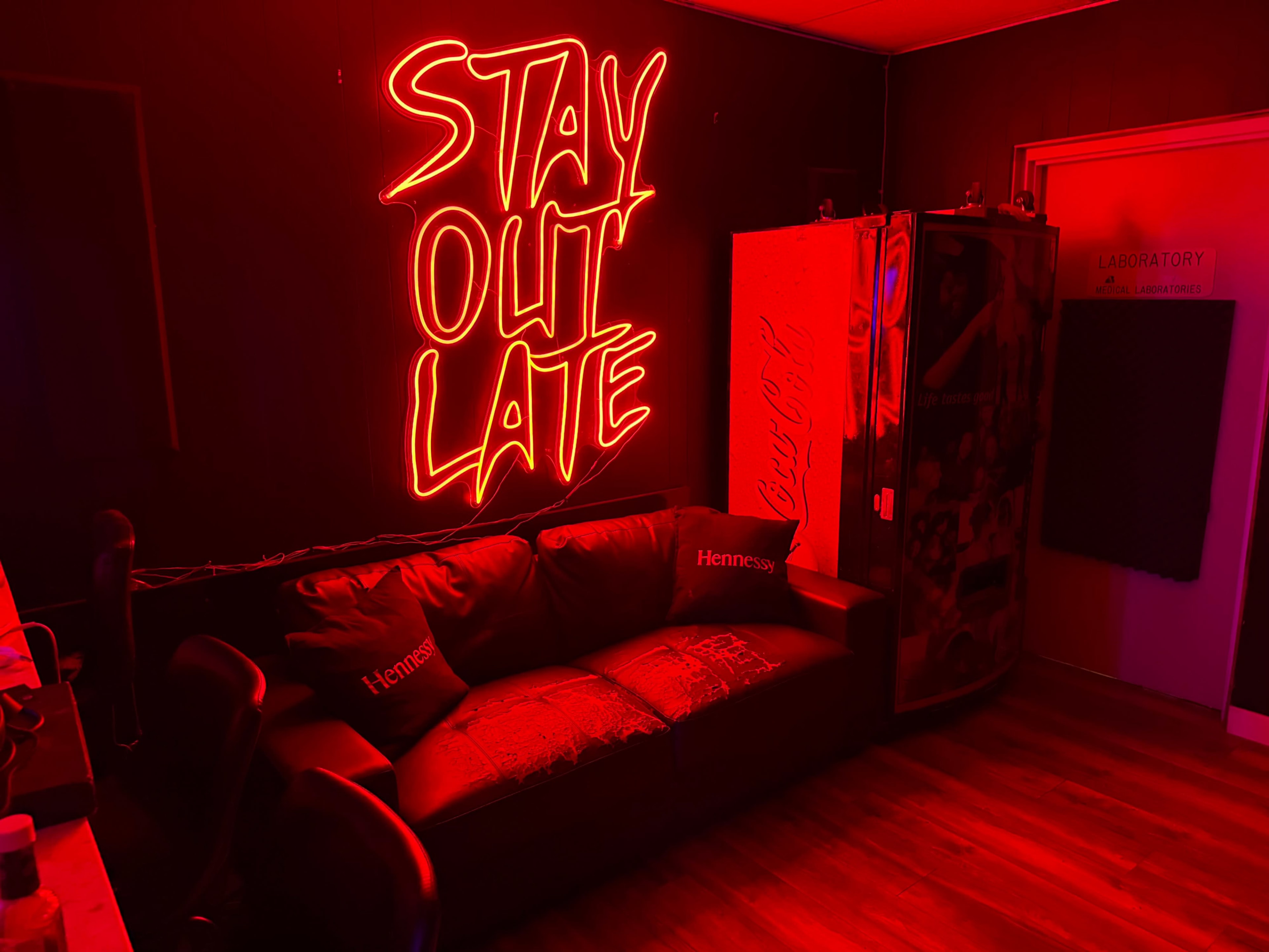 The image features a dimly lit room with a neon sign that reads "STAY OUT LATE," a dark sofa, and a door labeled "LABORATORY."