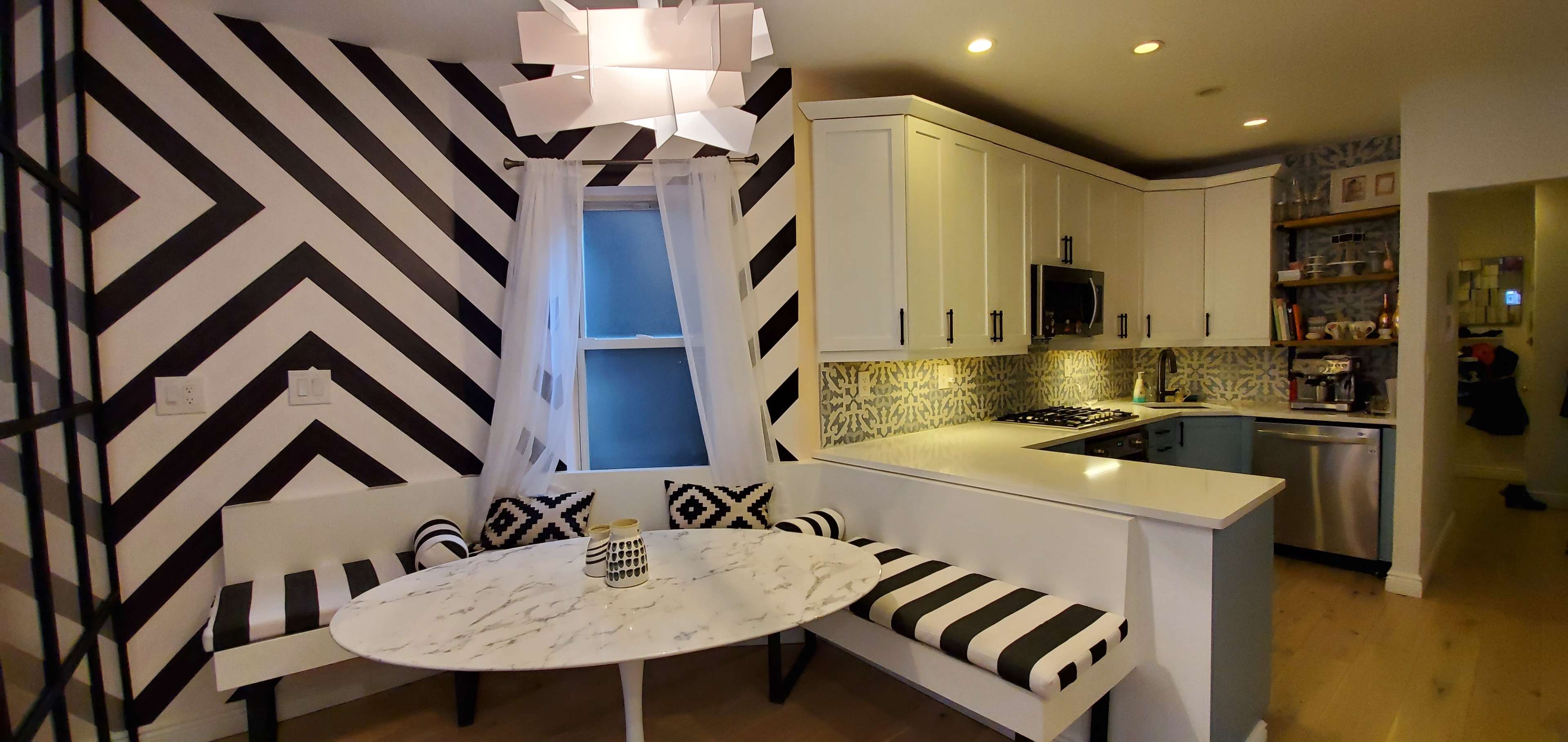 A modern kitchen featuring a round marble table with striped seating, white cabinetry, and a patterned wall in black and white.