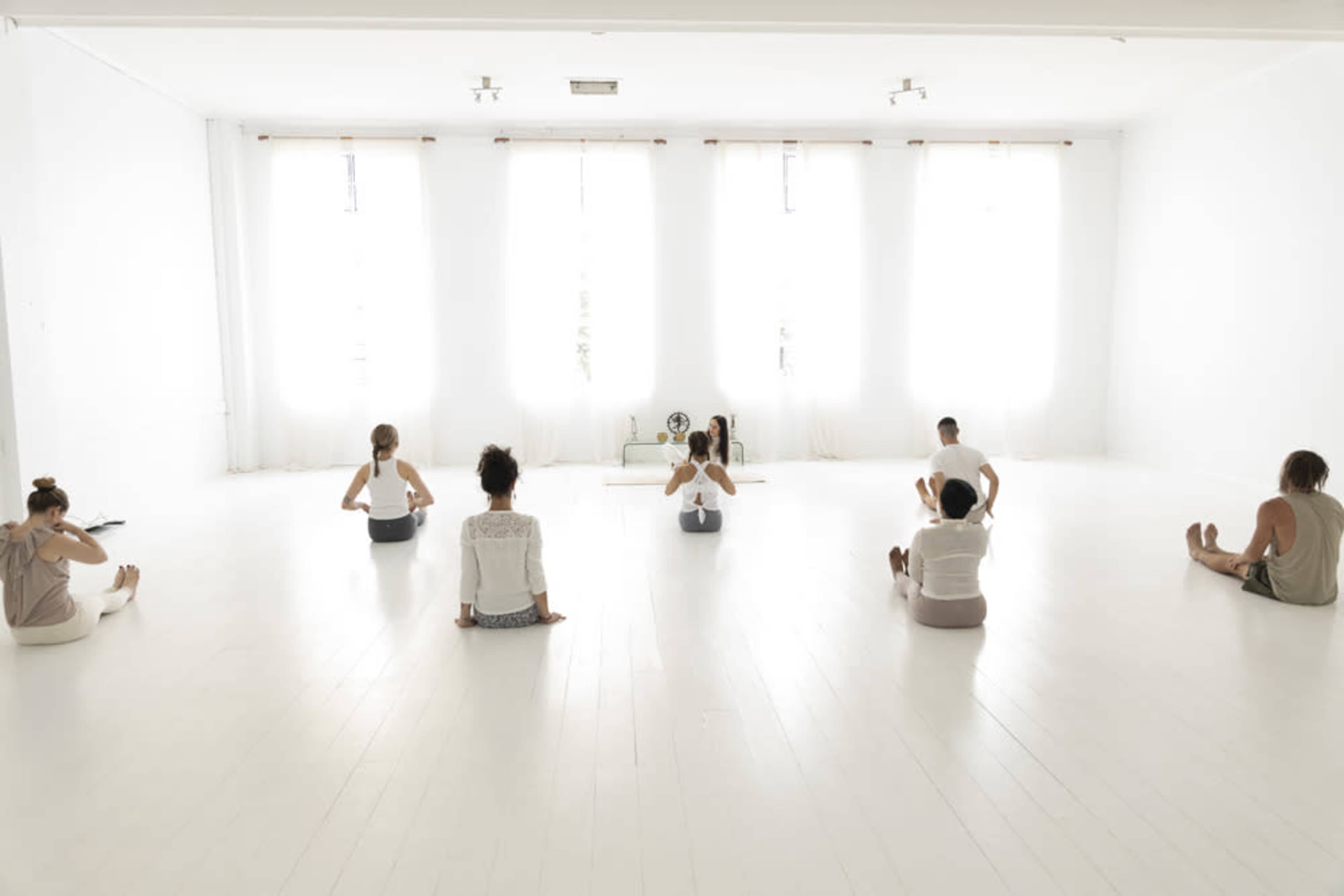 A group of individuals practices yoga in a brightly lit, spacious studio with large windows.