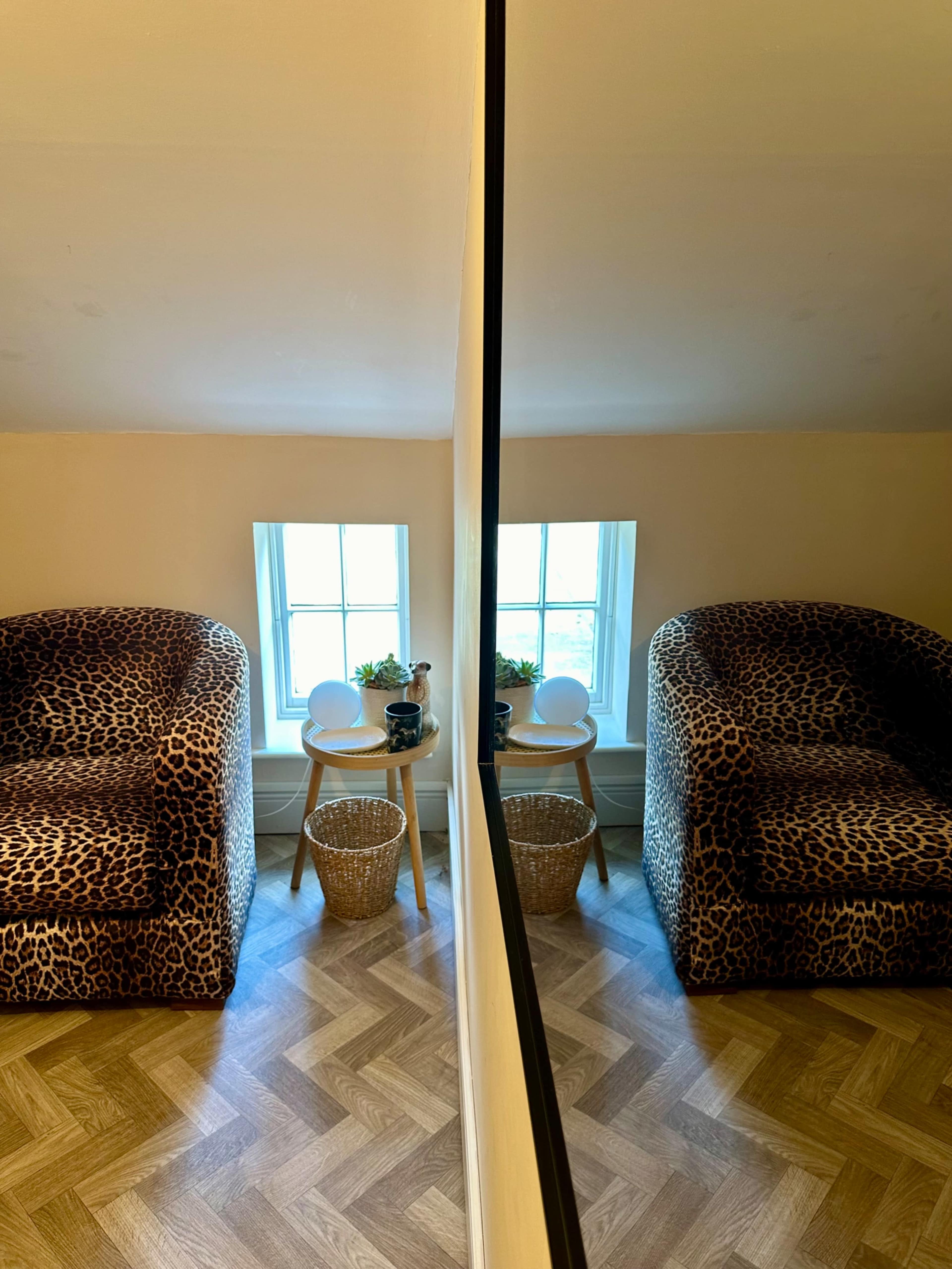 A room features a leopard-print chair next to a small table with a decorative item and a plant, reflected in a mirror.