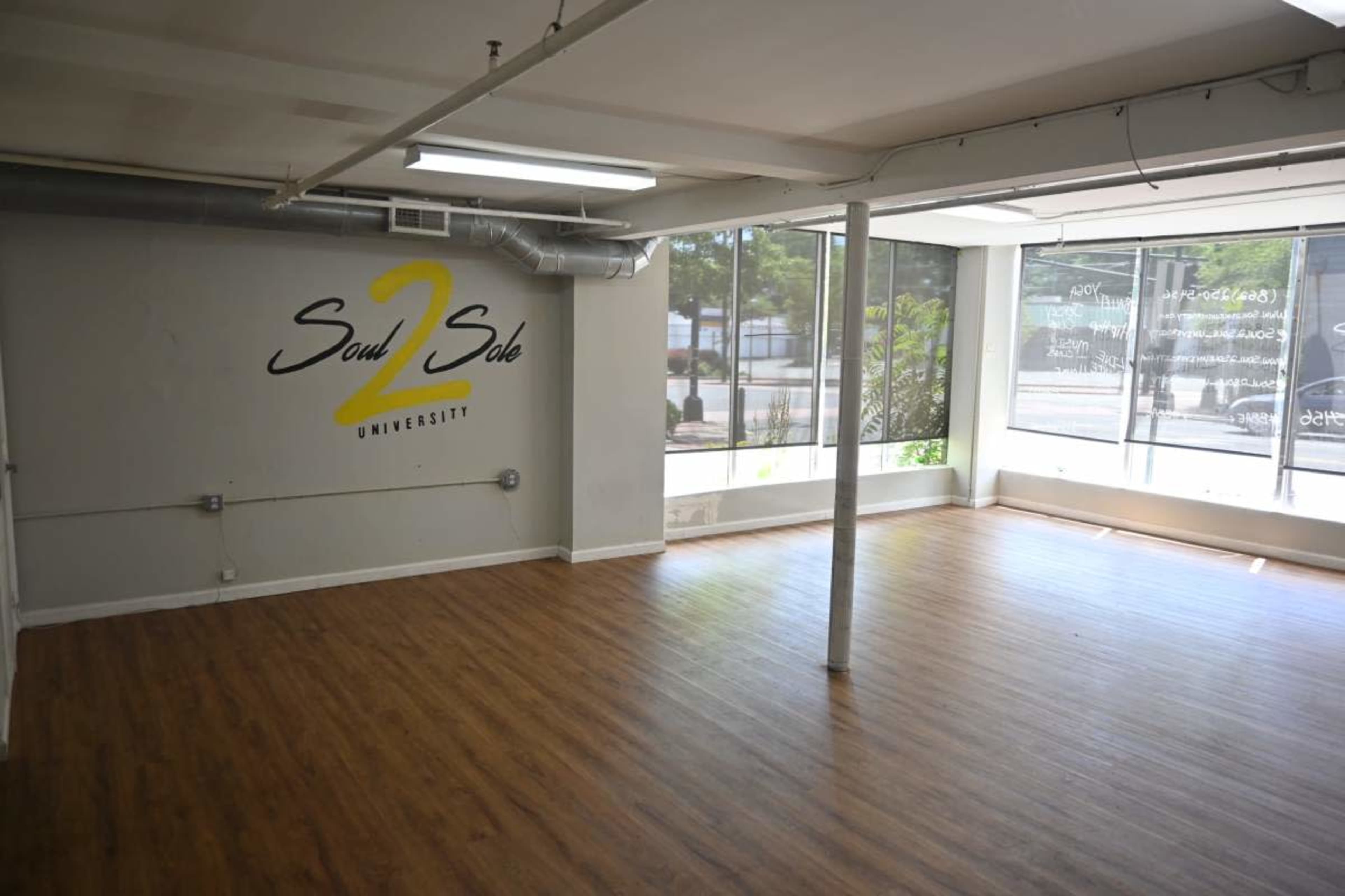 An empty studio space features wooden flooring and large windows, with the words "Soul 2 Sole University" displayed on a wall.