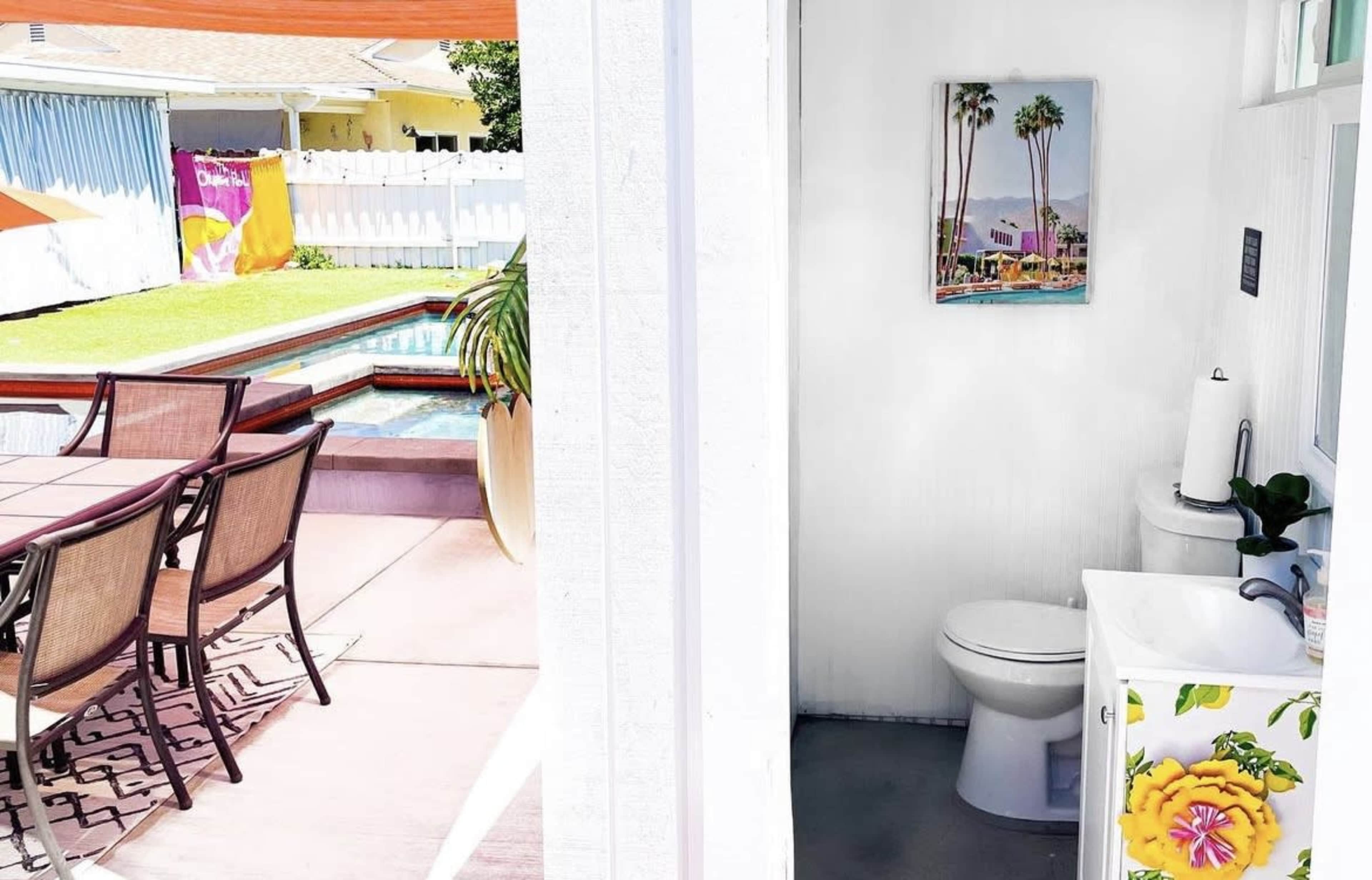 The image shows a bathroom area with a toilet and sink, viewed from an open doorway, next to a patio with a dining table and pool visible outside.