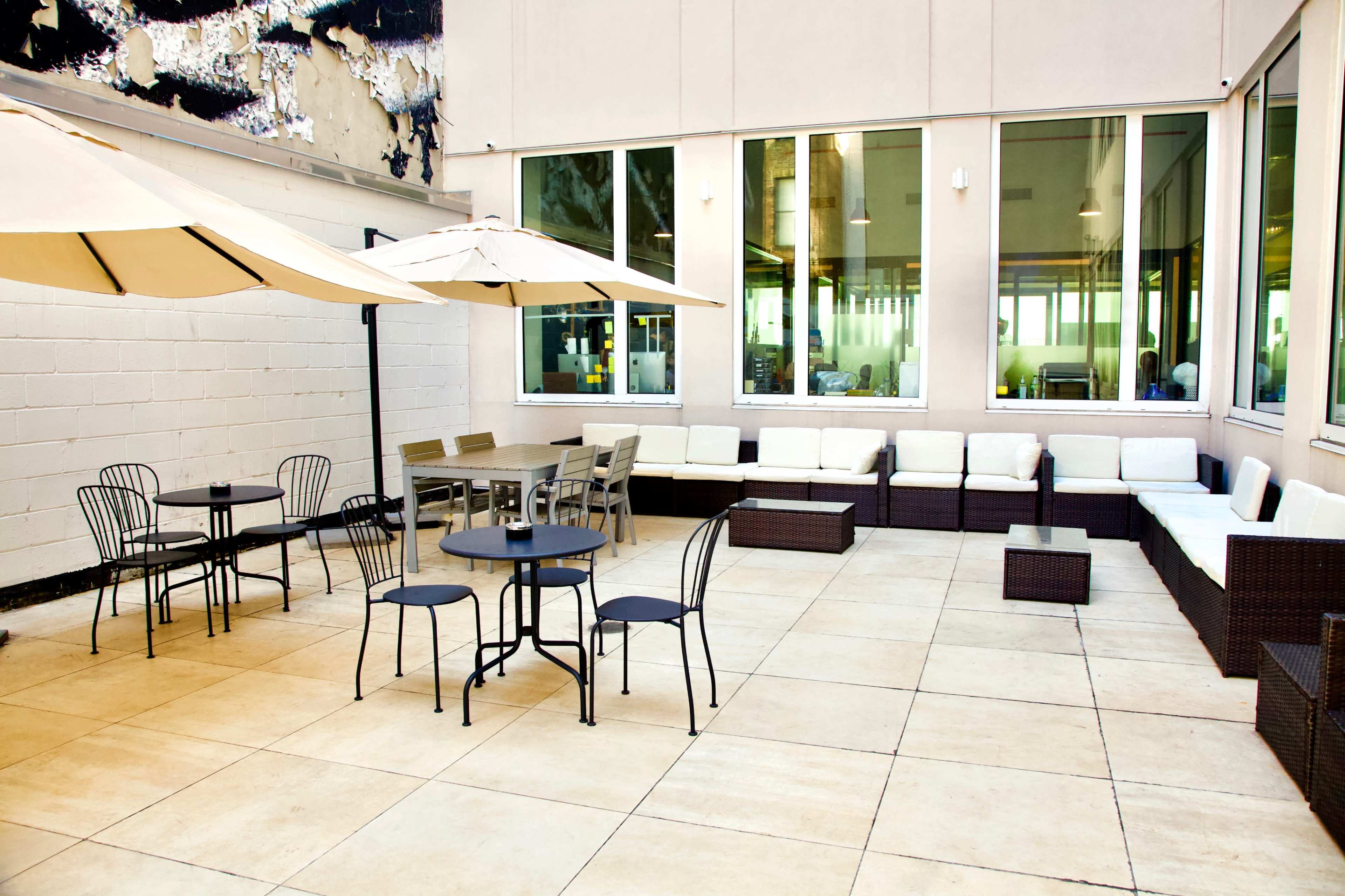 A spacious patio area with several tables and chairs, umbrellas for shade, and a seating arrangement against a wall.