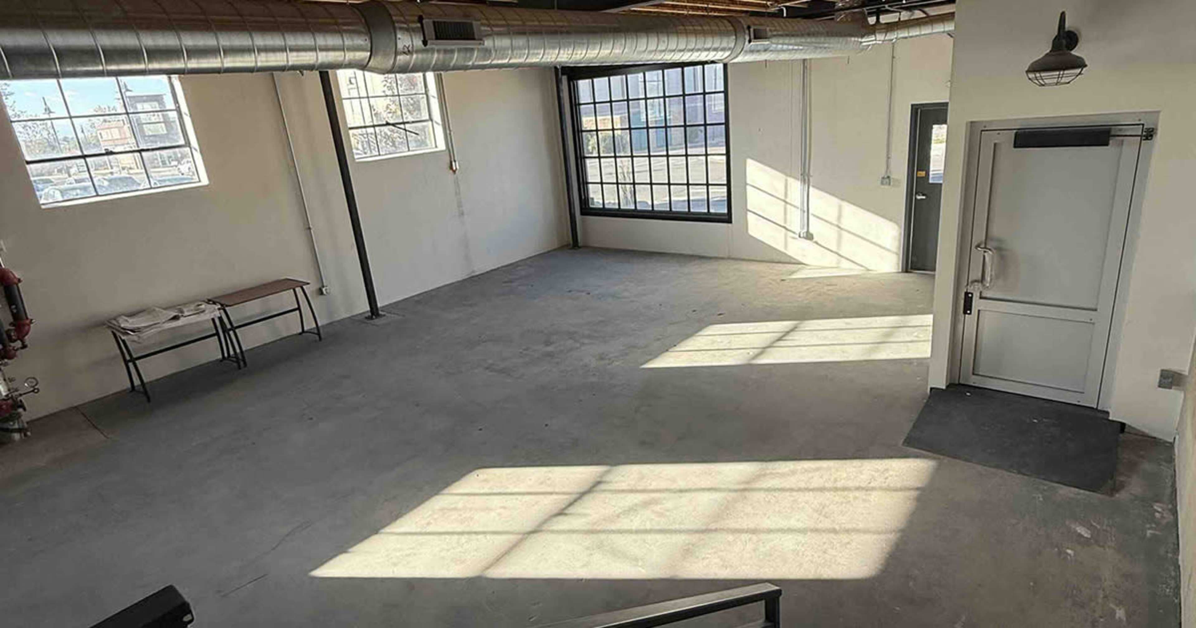 The image shows an empty room with large windows allowing sunlight to cast shadows on the concrete floor.
