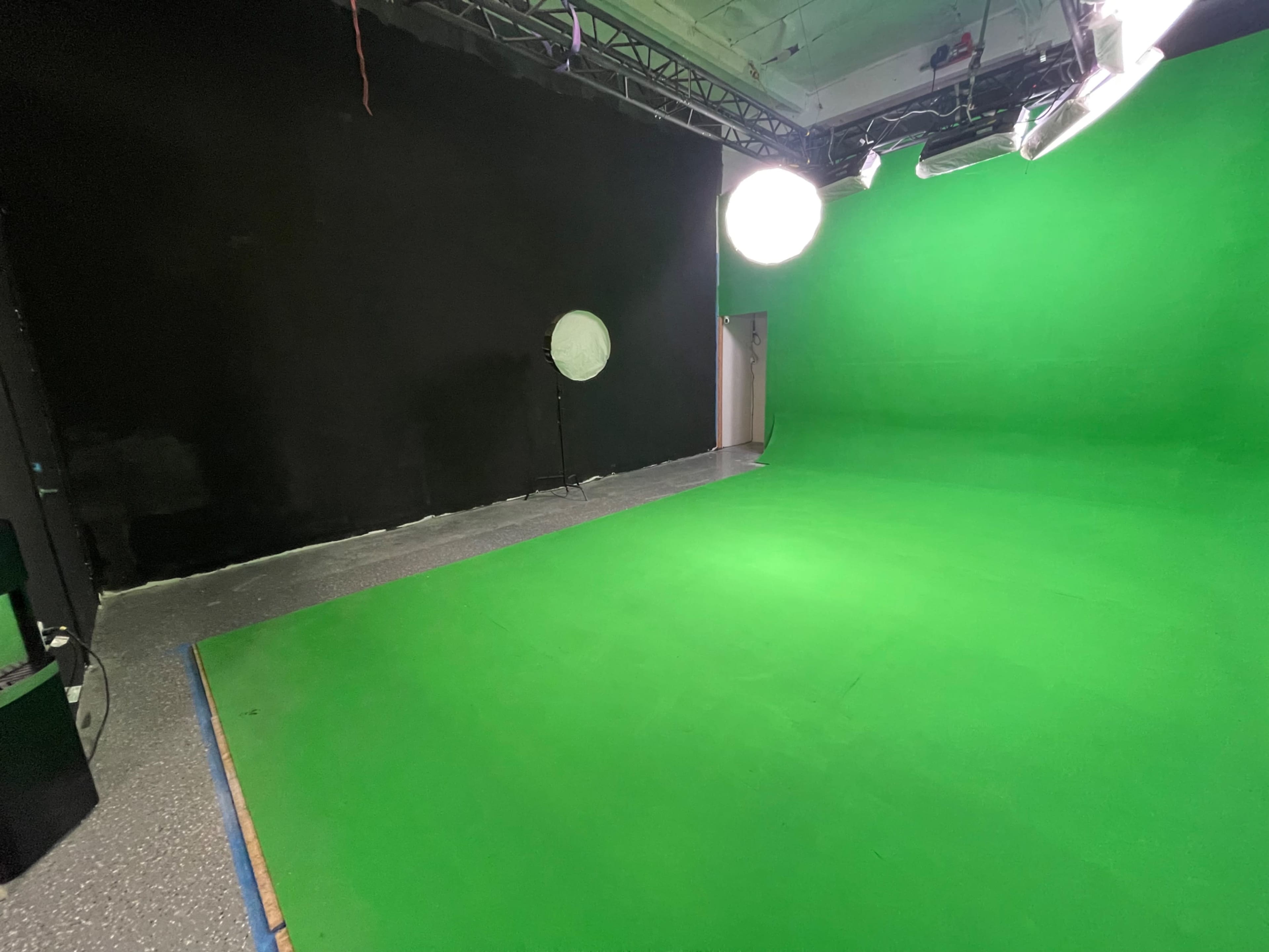 The image shows a green screen studio with a green backdrop, a circular light, and a black wall in the background.