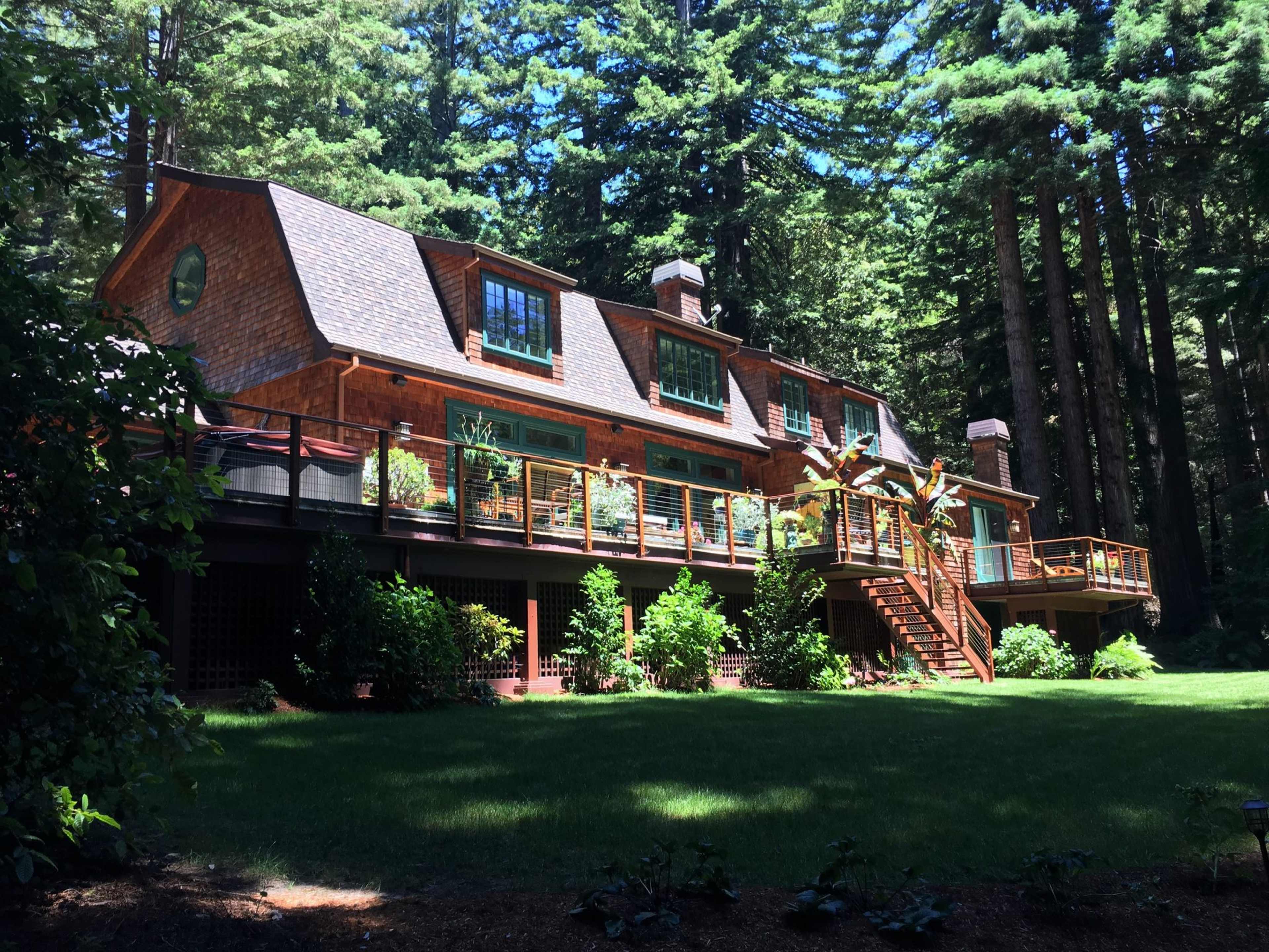 A large wooden house with multiple windows and a deck surrounded by tall green trees.