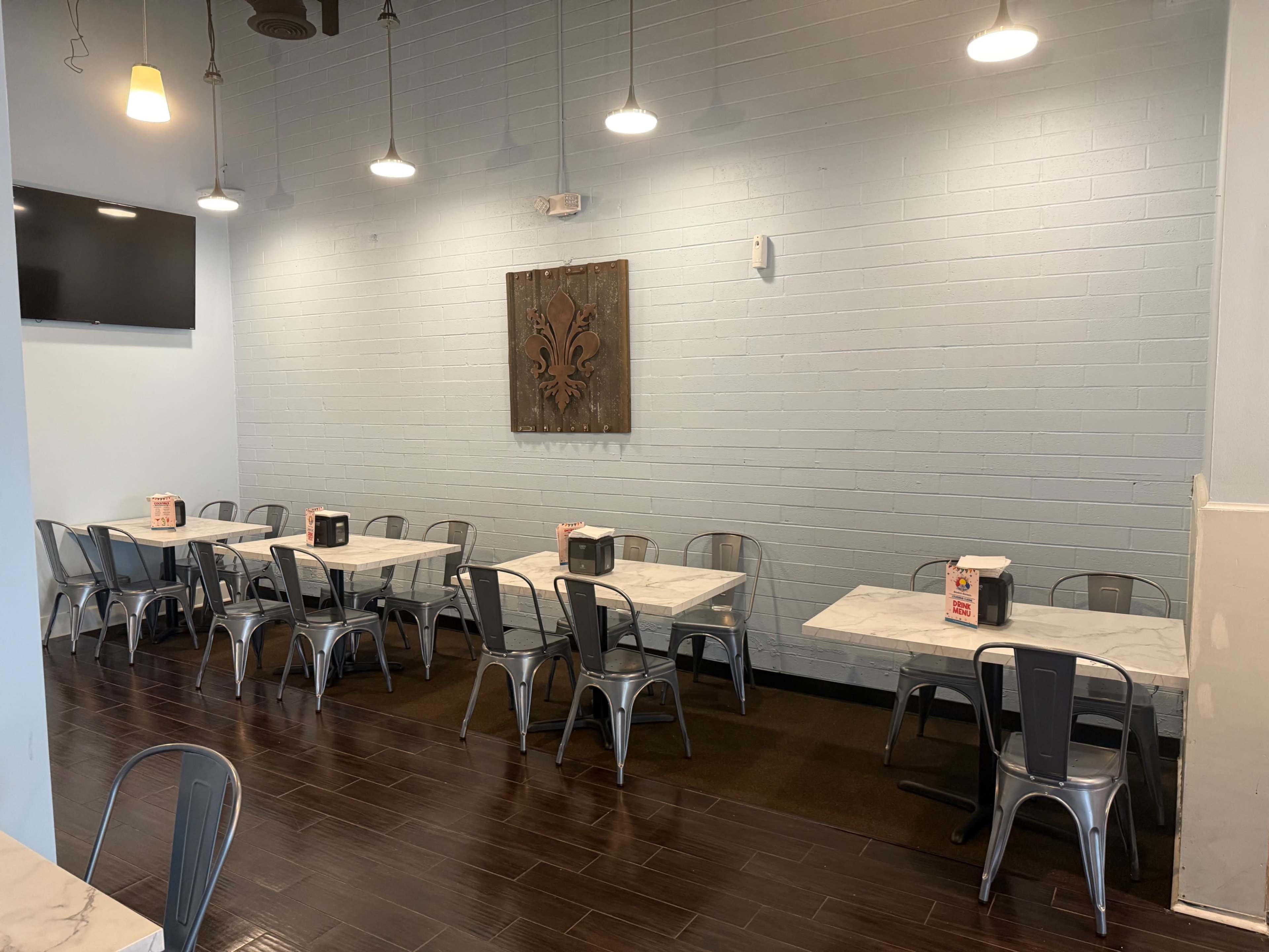 The image shows a dining area with several marble-topped tables and metal chairs arranged neatly against light blue walls, featuring a decorative wall piece and overhead lighting.