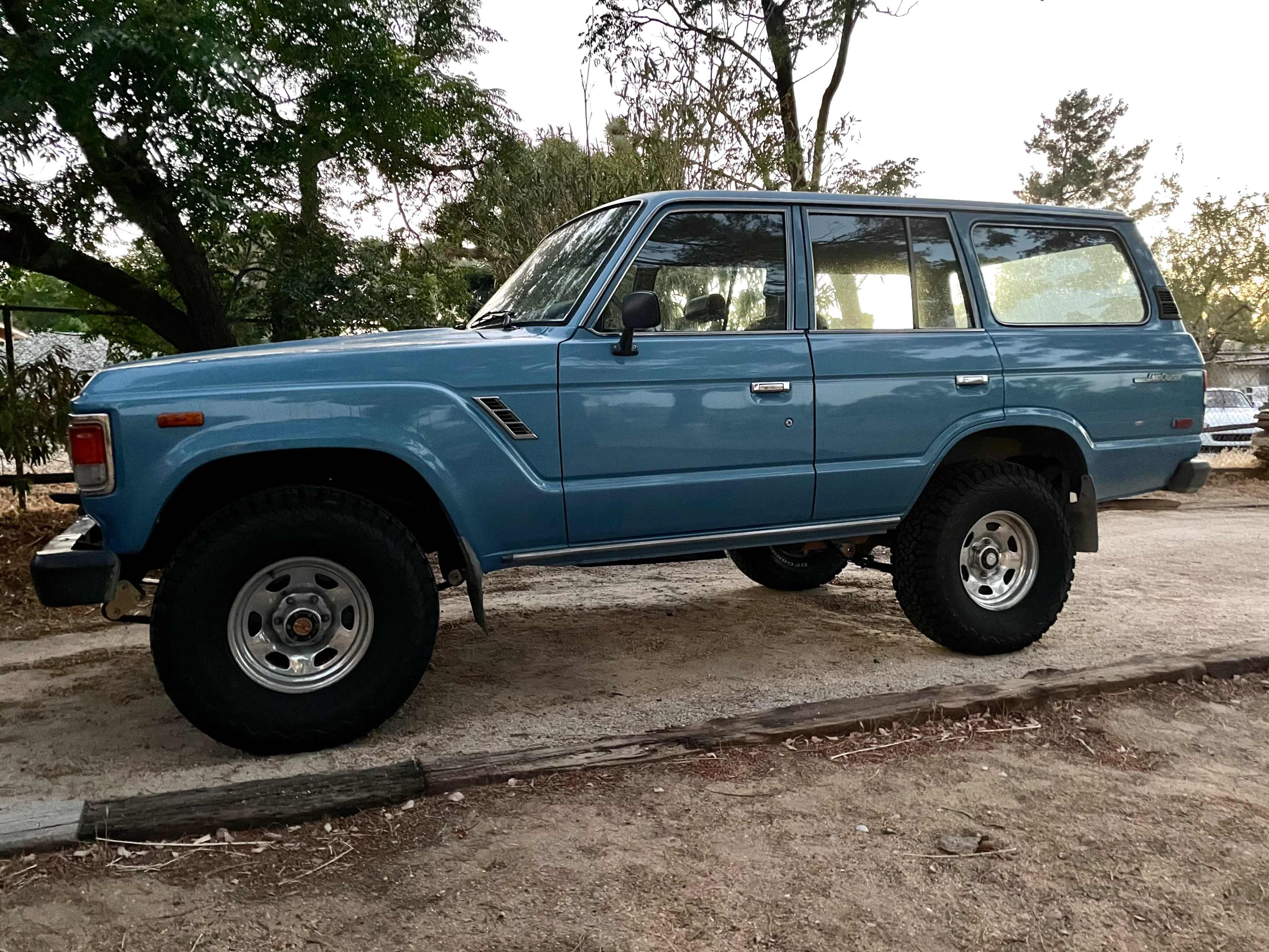 A blue vintage SUV parked on a dirt road surrounded by trees.
