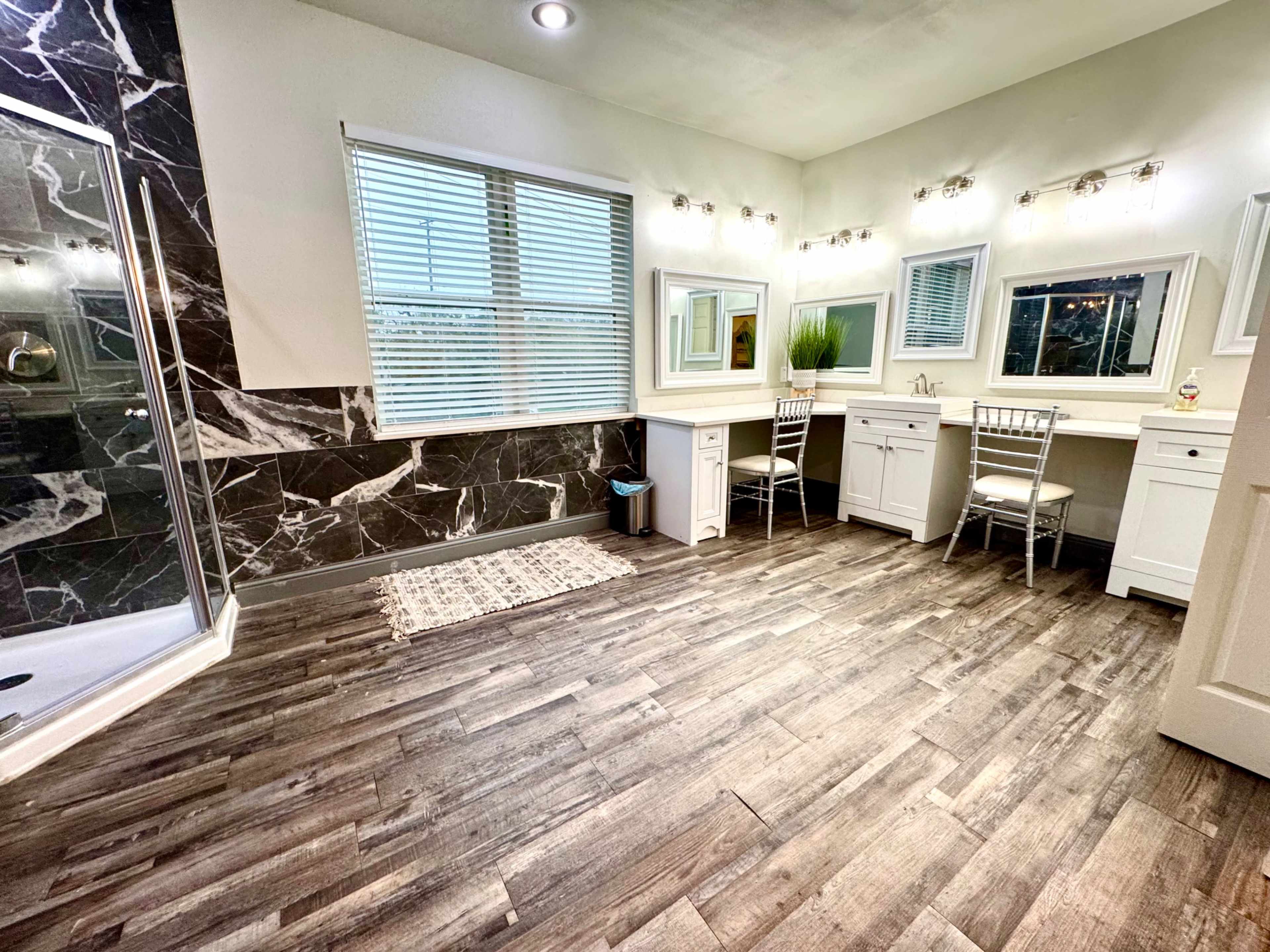 The image shows a modern bathroom with a separate shower area, a large vanity with mirrors and lighting, and wooden flooring.