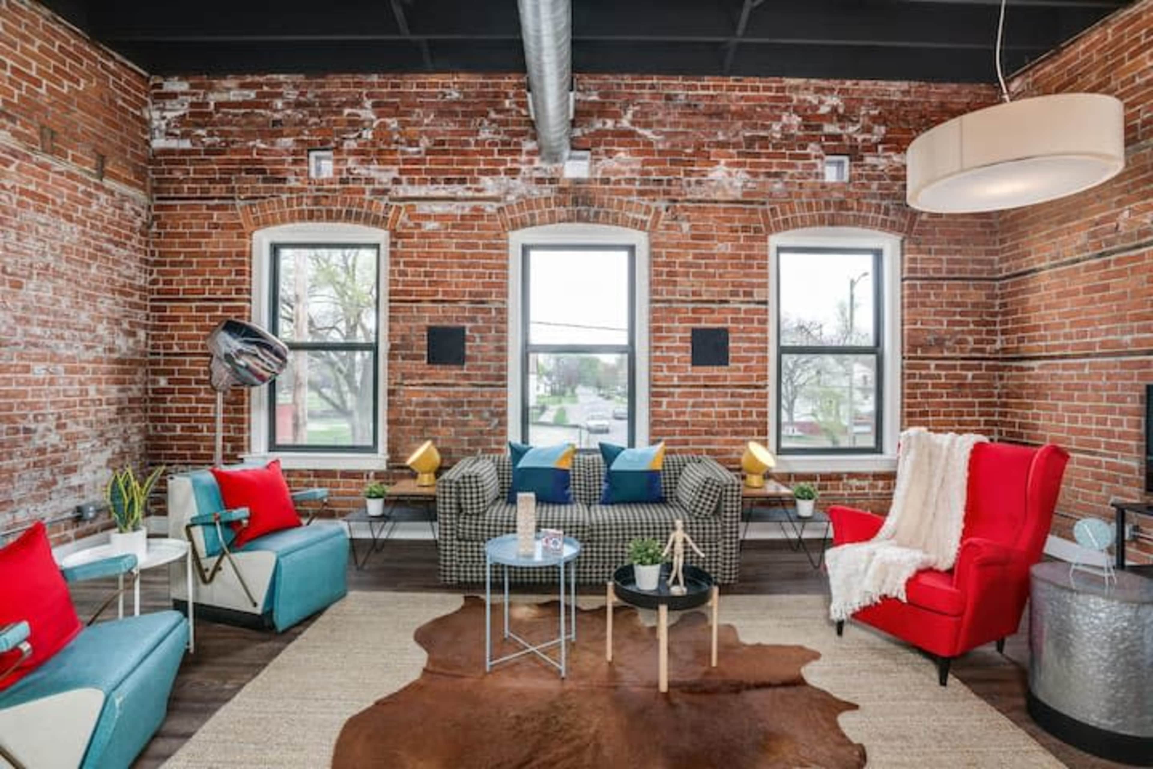 A stylish living room with exposed brick walls, large windows, and modern furniture arranged around a central coffee table.