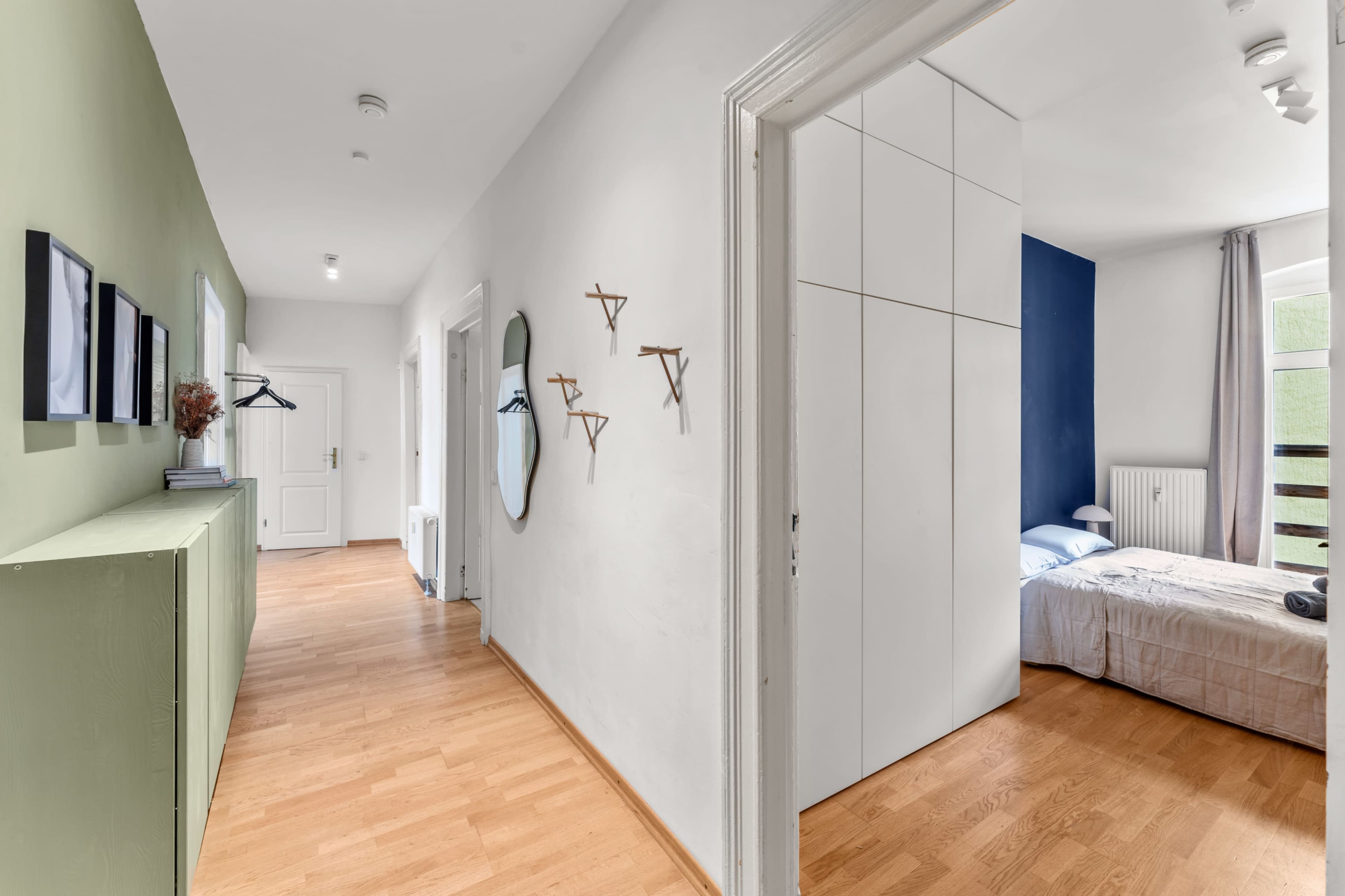 A hallway leads to a bedroom with a green accent wall and simple furniture.