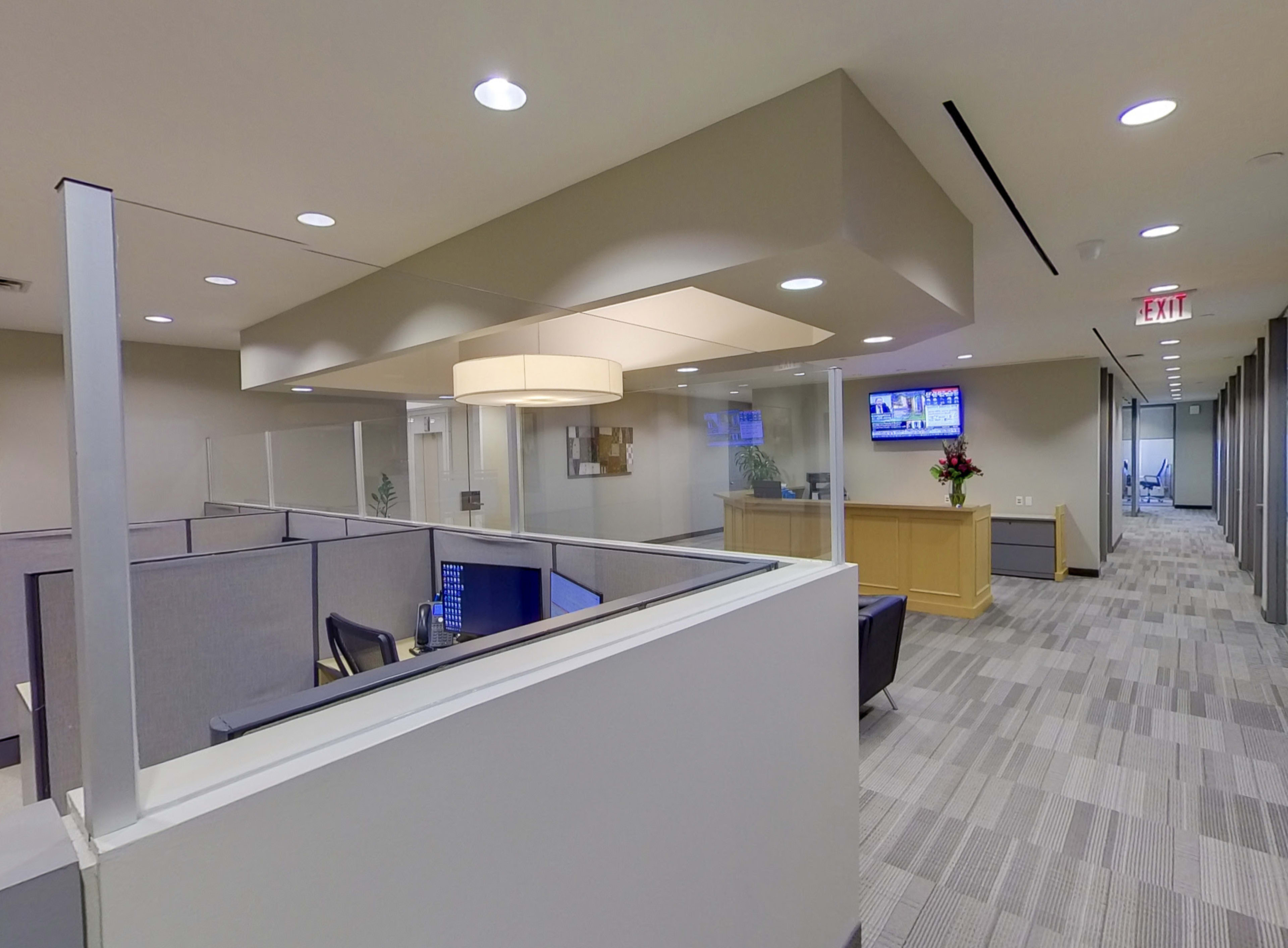 The image shows a modern office space with cubicles, a reception area, and a television display.