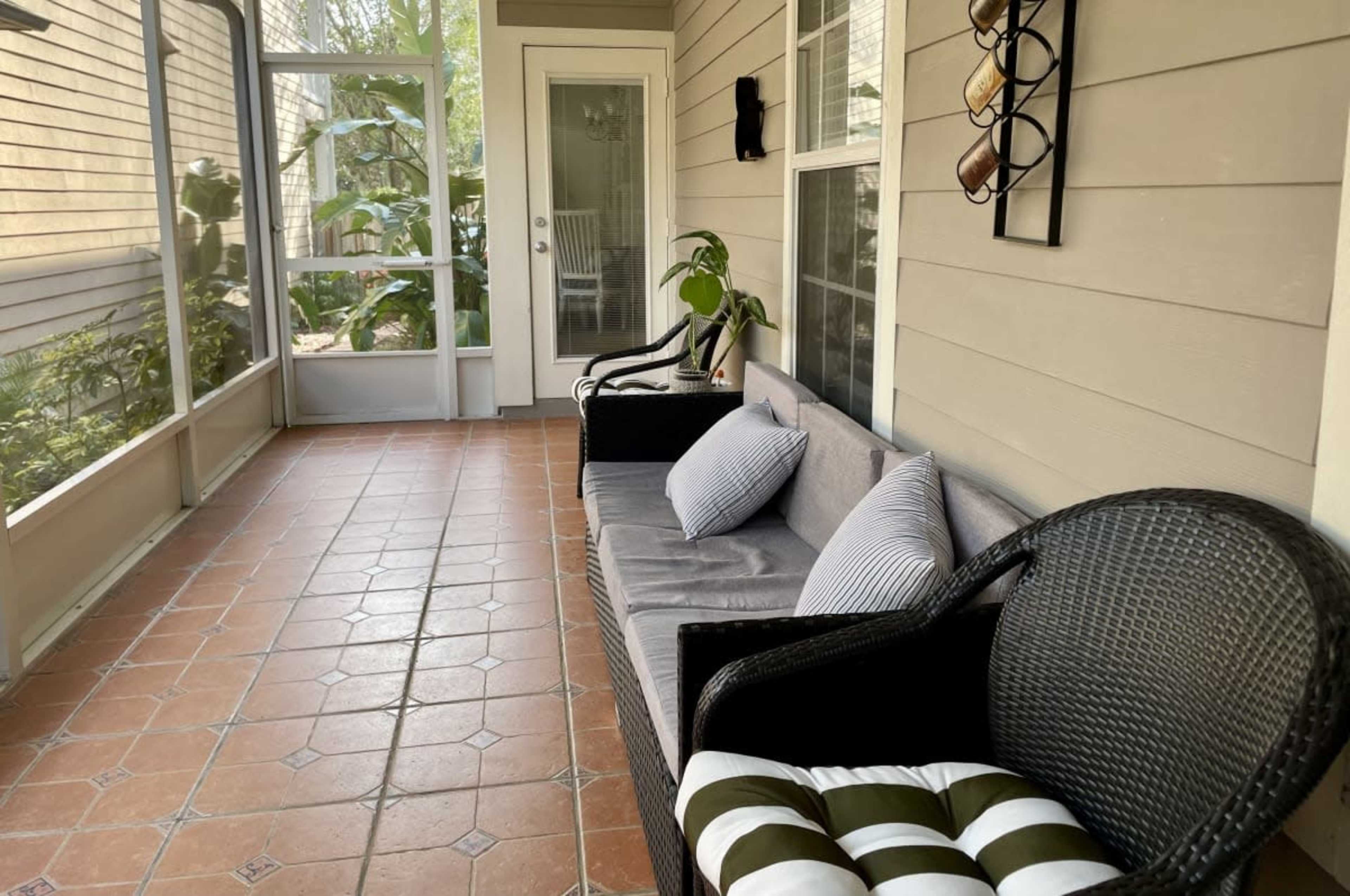 The image shows a screened porch featuring two wicker chairs with decorative cushions and a tiled floor.