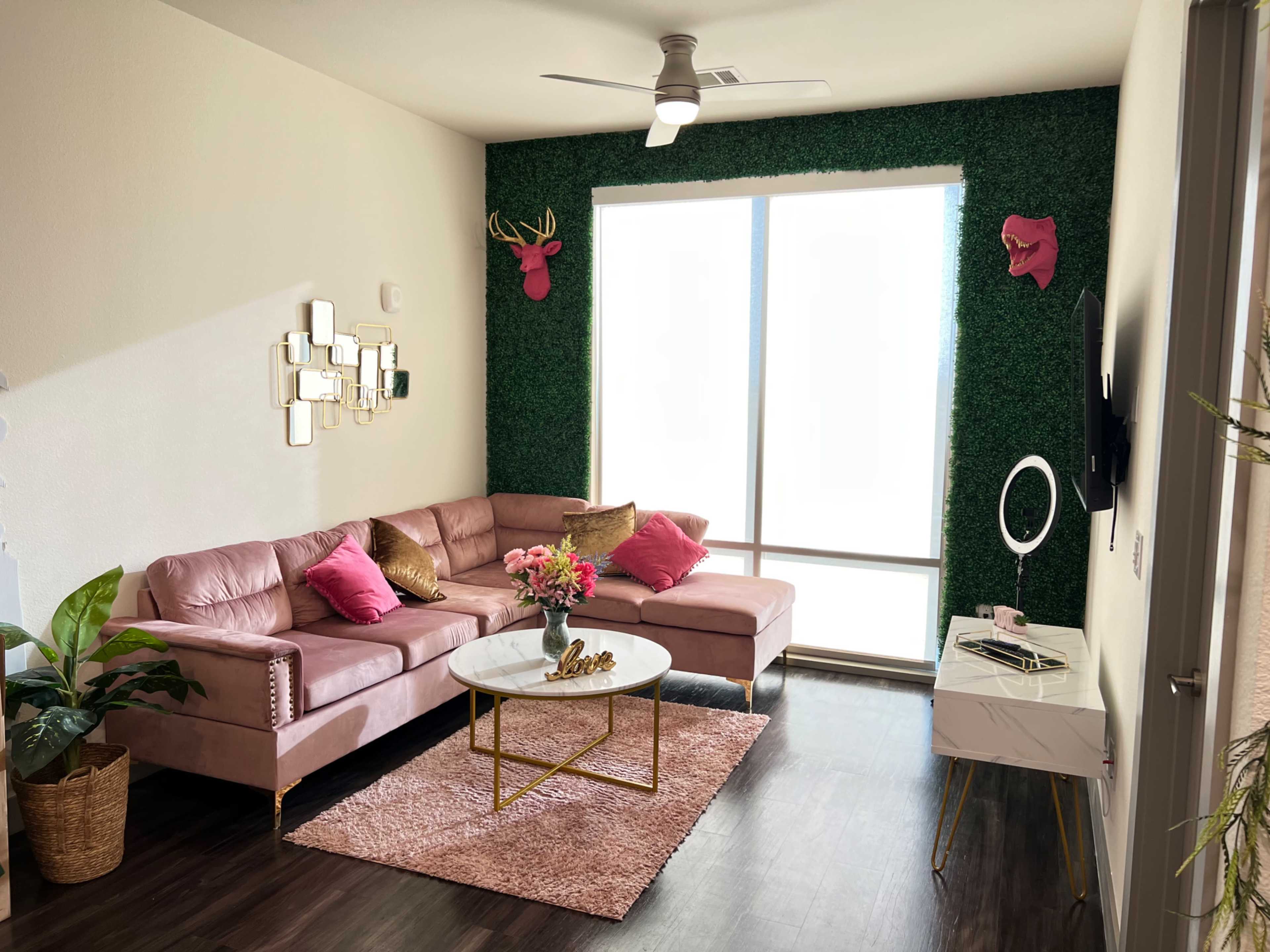 A modern living room with a pink sectional sofa, a round coffee table, and decorative elements including wall-mounted deer heads and a green wall accent.