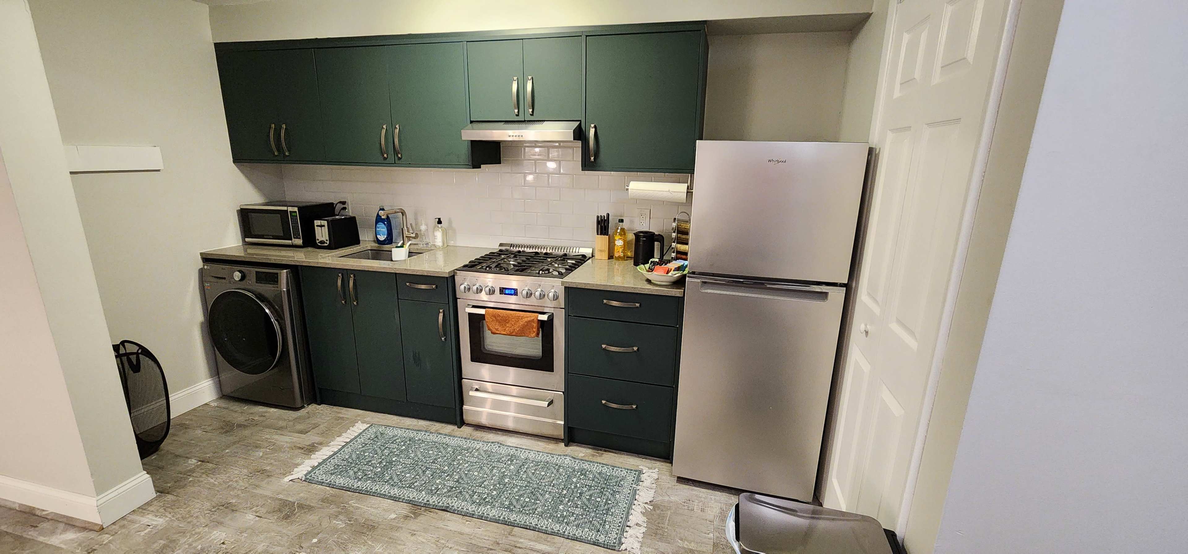 A modern kitchen featuring dark green cabinets, stainless steel appliances, and a laundry machine.