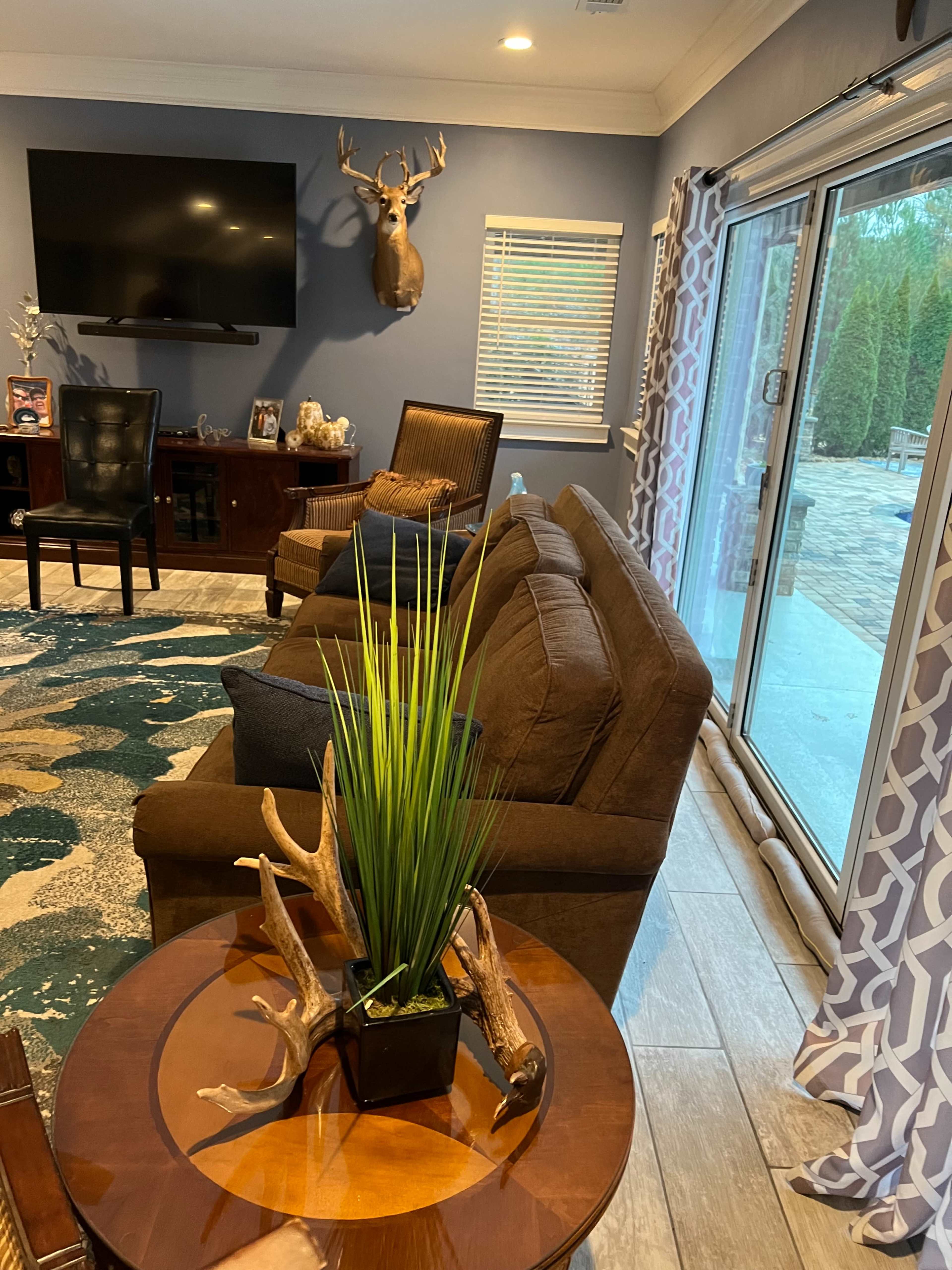 A living room features a brown sofa, an antler-mounted deer head on the wall, and a table with a potted plant and decorative antlers.