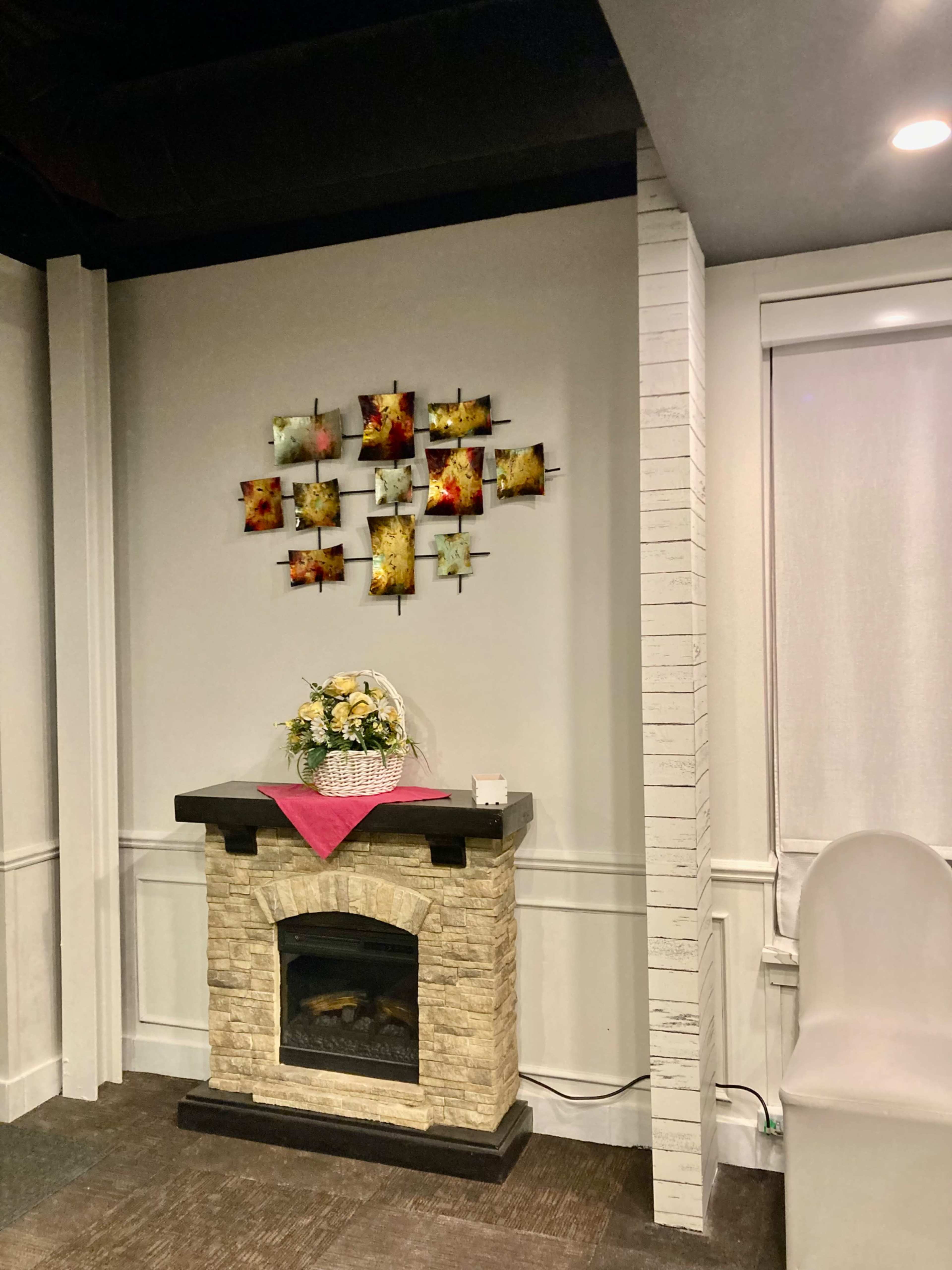 A cozy room featuring a stone fireplace with a decorative arrangement of framed artwork above it, and a bouquet of flowers on a table in front.