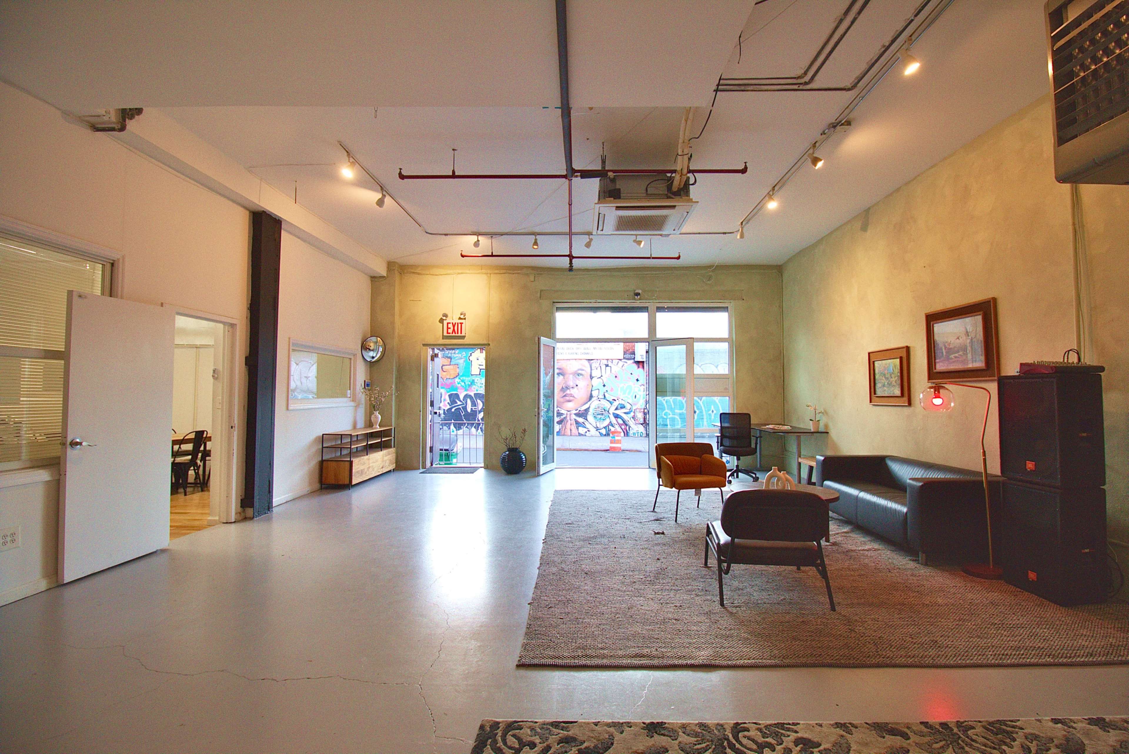 The image shows a spacious, modern studio apartment with a large window and an exit leading to a vibrant mural outside.