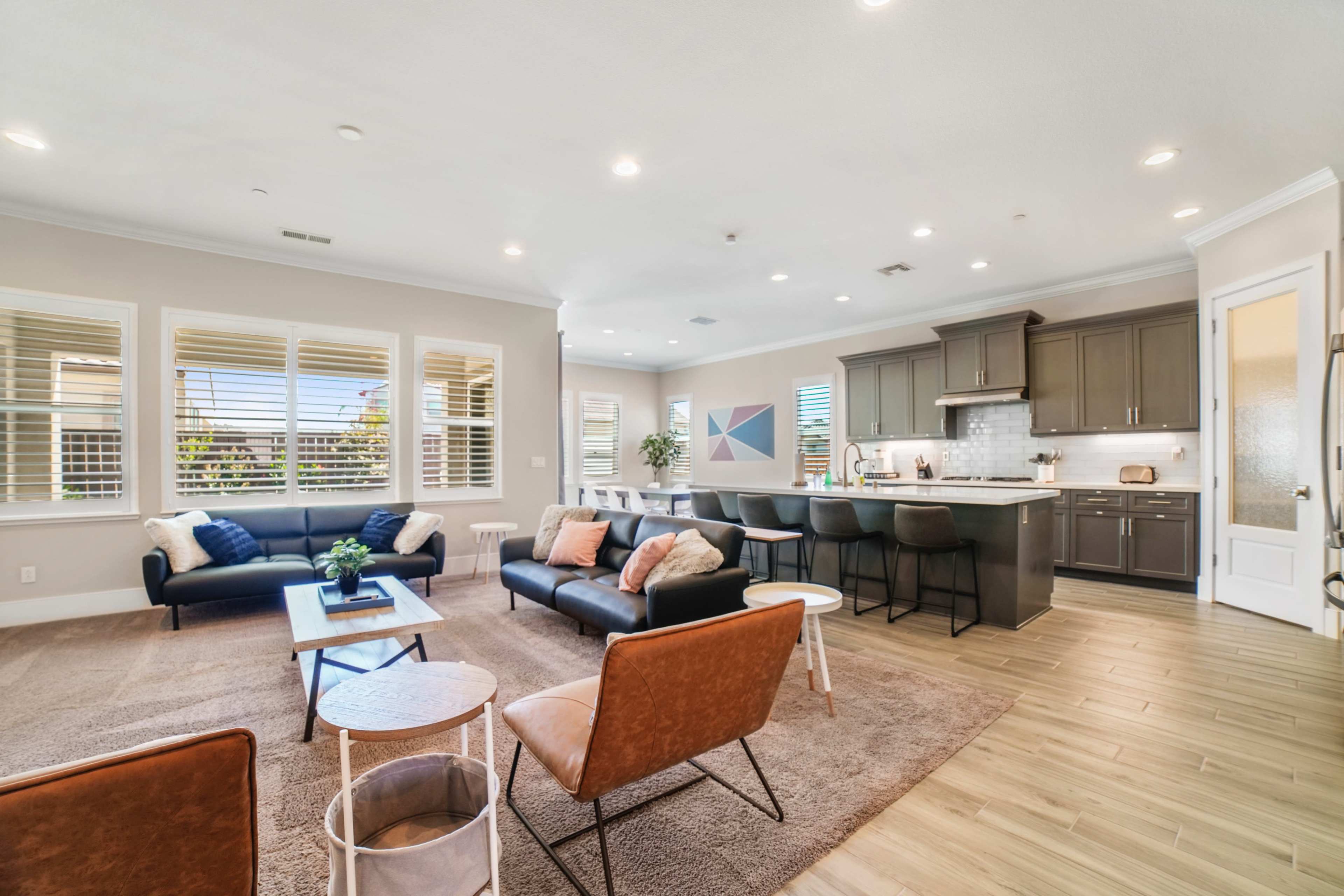 A modern living room and kitchen area with seating, large windows, and a neutral color palette.