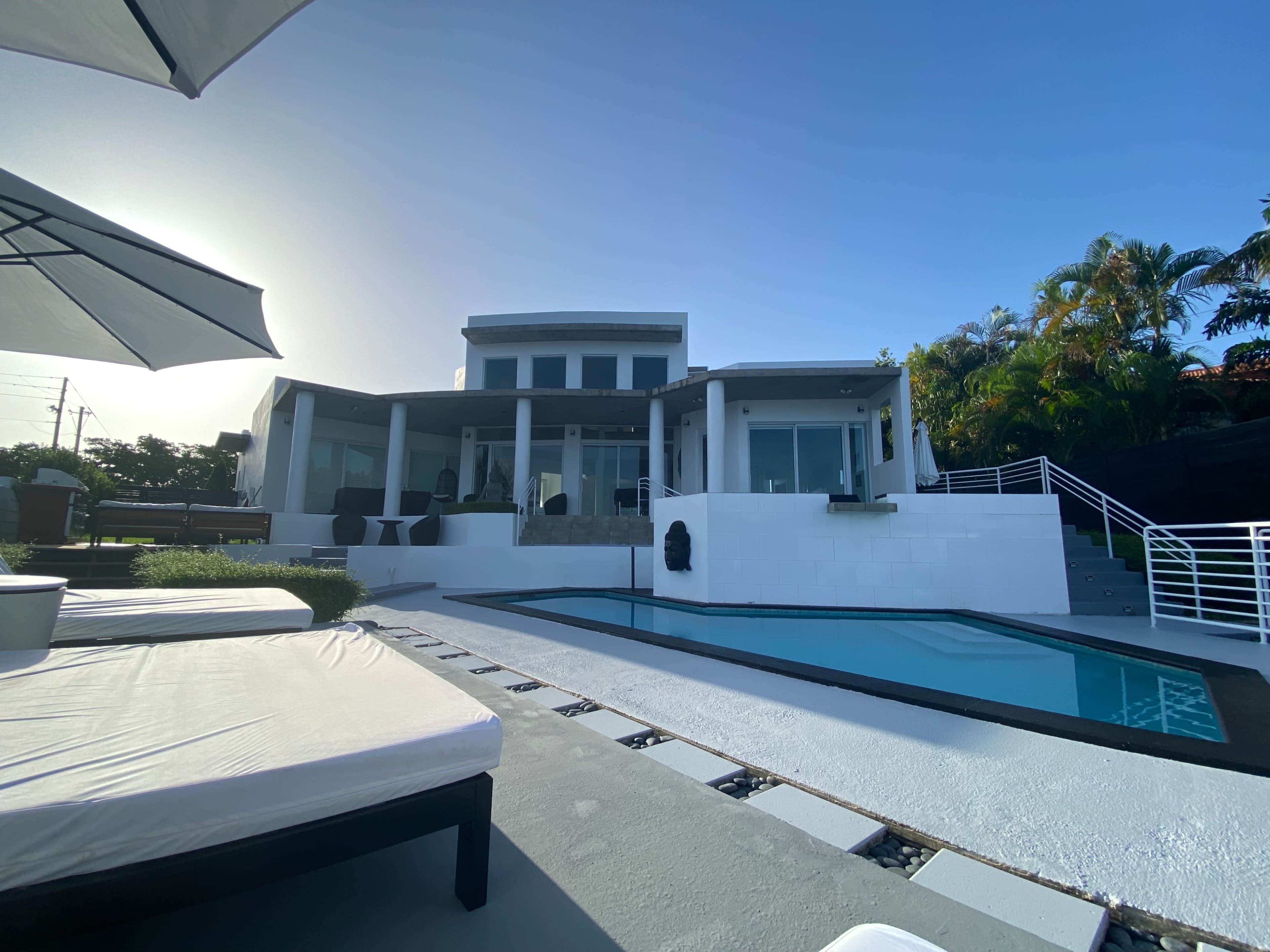 A modern house with large glass windows overlooks a swimming pool and a landscaped yard.