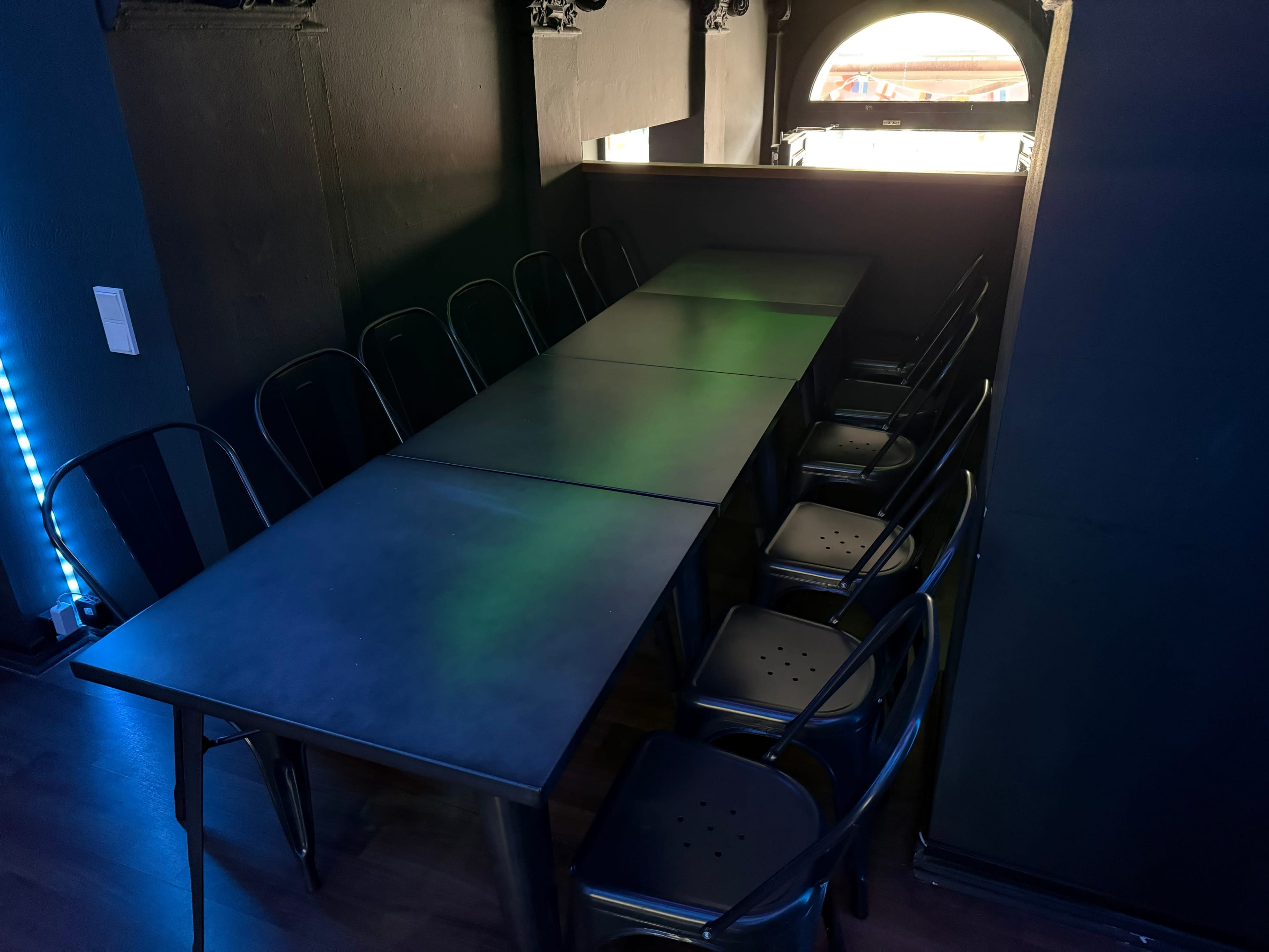 A long, rectangular black table with several black chairs is set in a dimly lit room featuring an arched window.