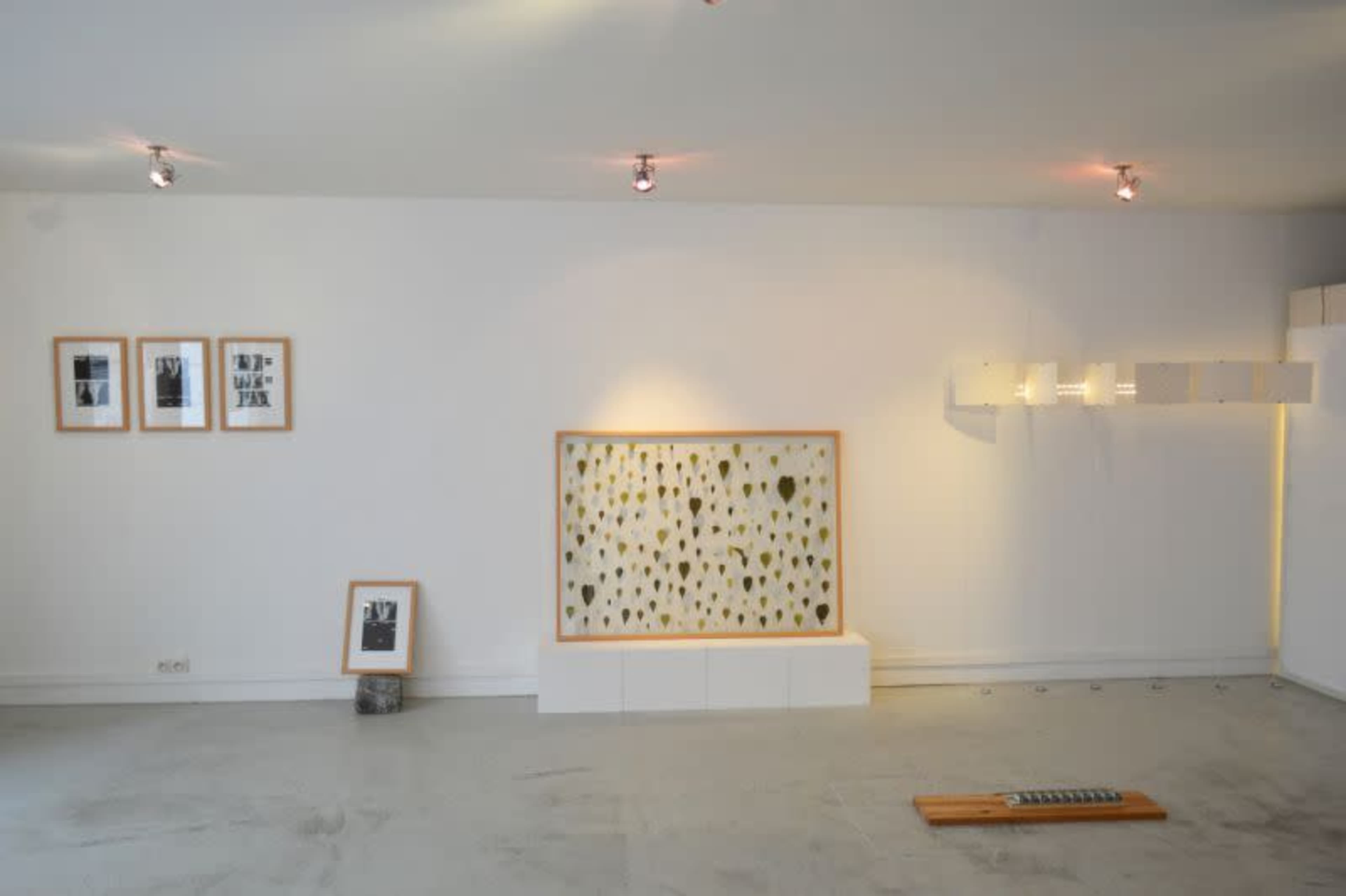 The image depicts an art gallery with framed black-and-white photographs on the left and a large piece of artwork featuring yellow and green spots on the right, set against a white wall.
