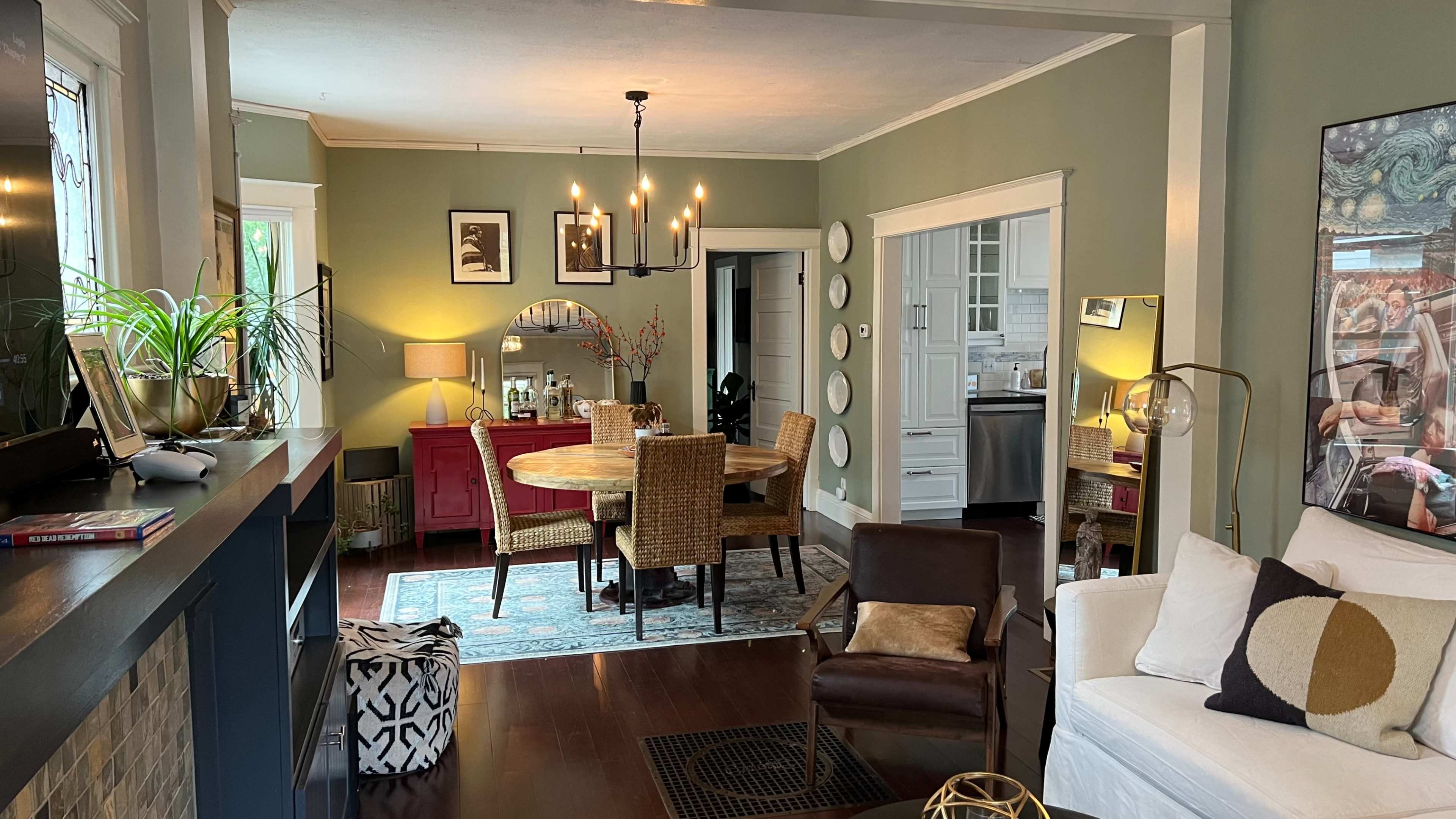 The image shows a modern, light-filled living room with a dining area featuring a round table surrounded by wicker chairs, a brown leather chair, and a white sofa.