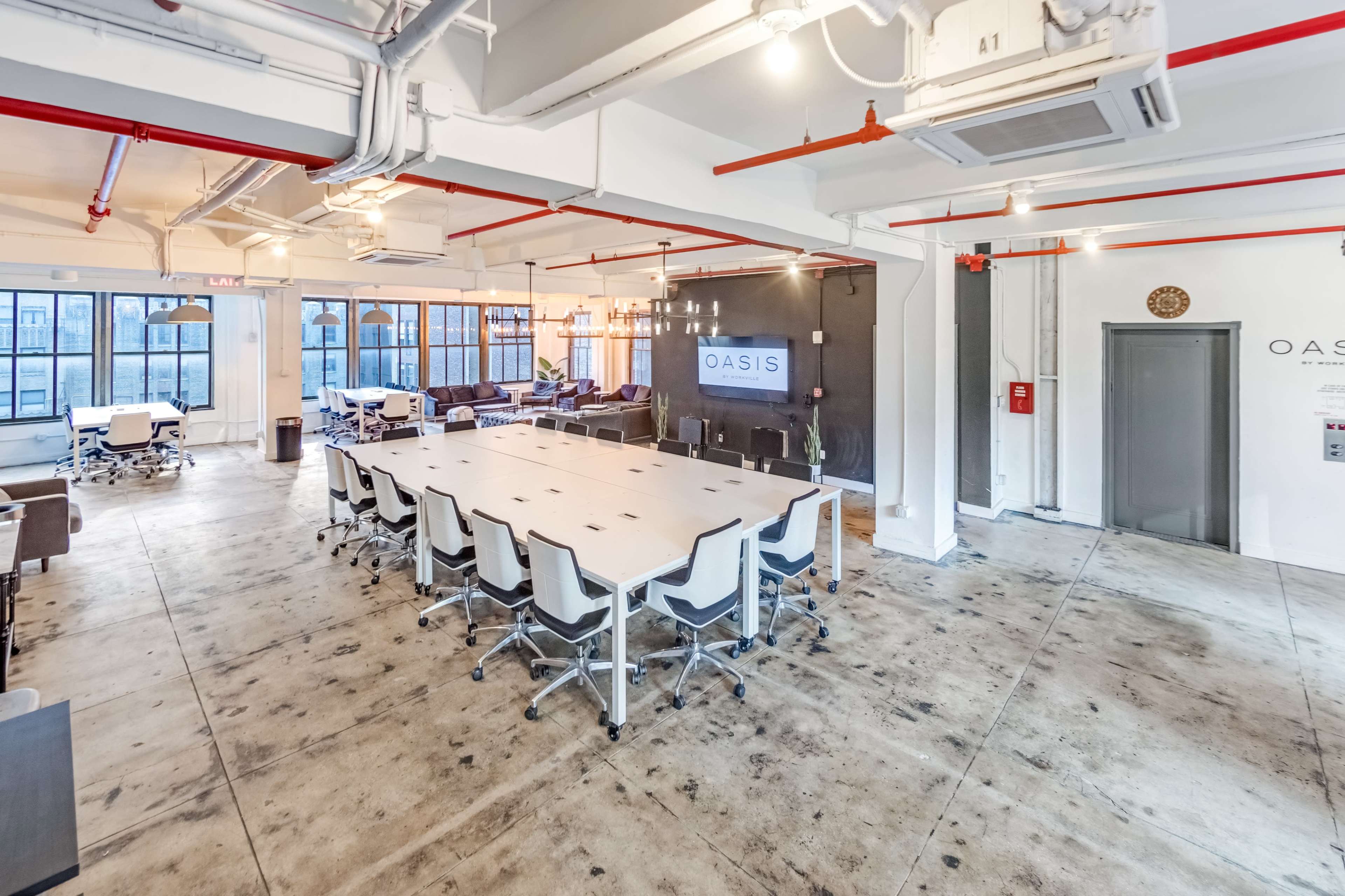 A spacious, modern co-working office with a large conference table, multiple workstations, and large windows allowing natural light.