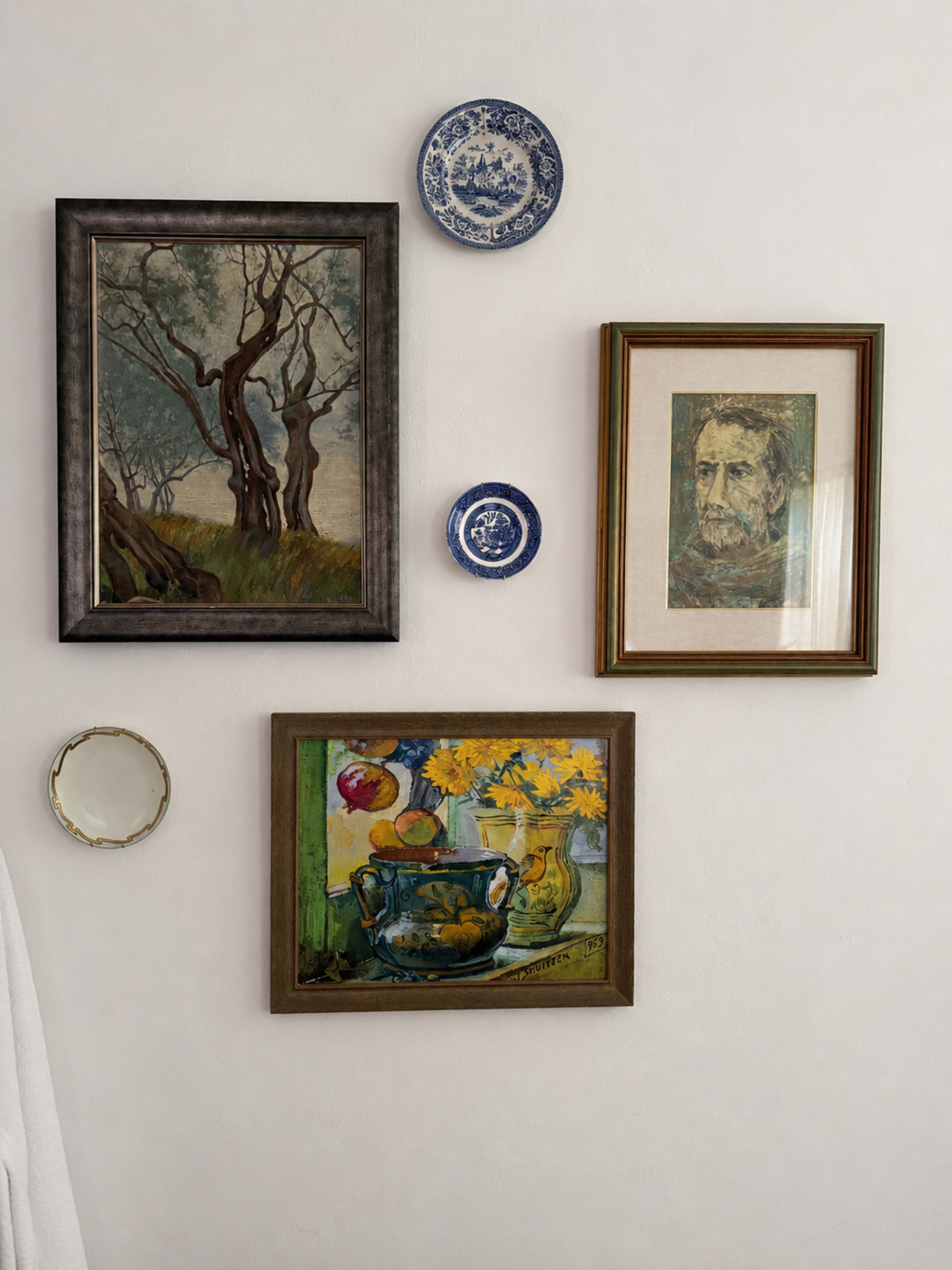 The scene features a wall adorned with four framed artworks and decorative plates, including a painting of trees, a portrait, and a still life with a vase of flowers.