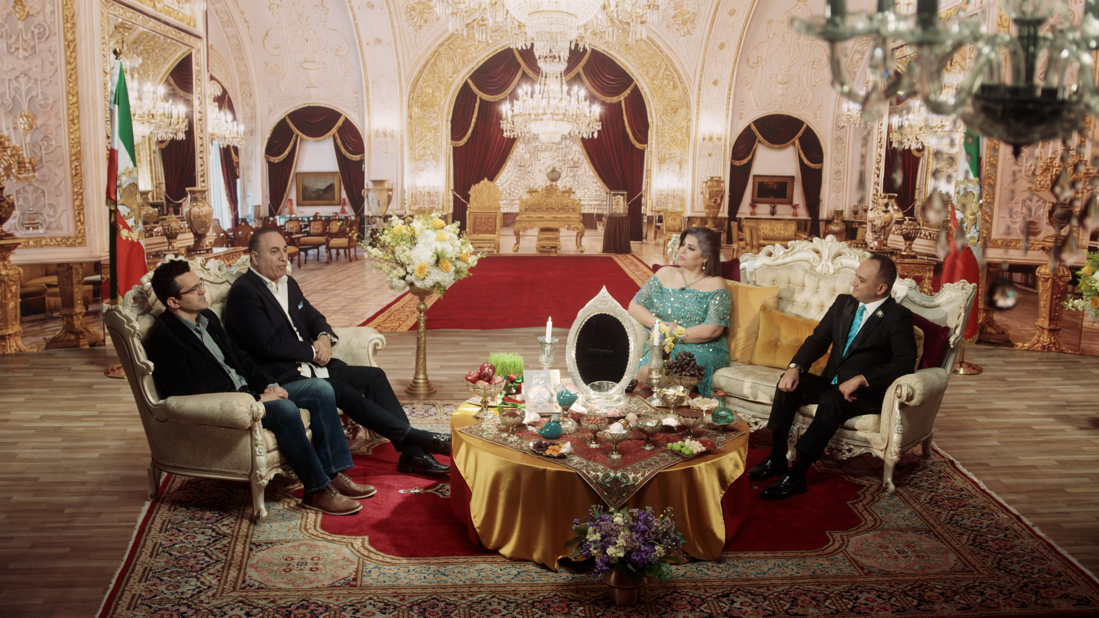 A group of four people sits in an elaborately decorated room featuring luxurious furnishings and ornate details.