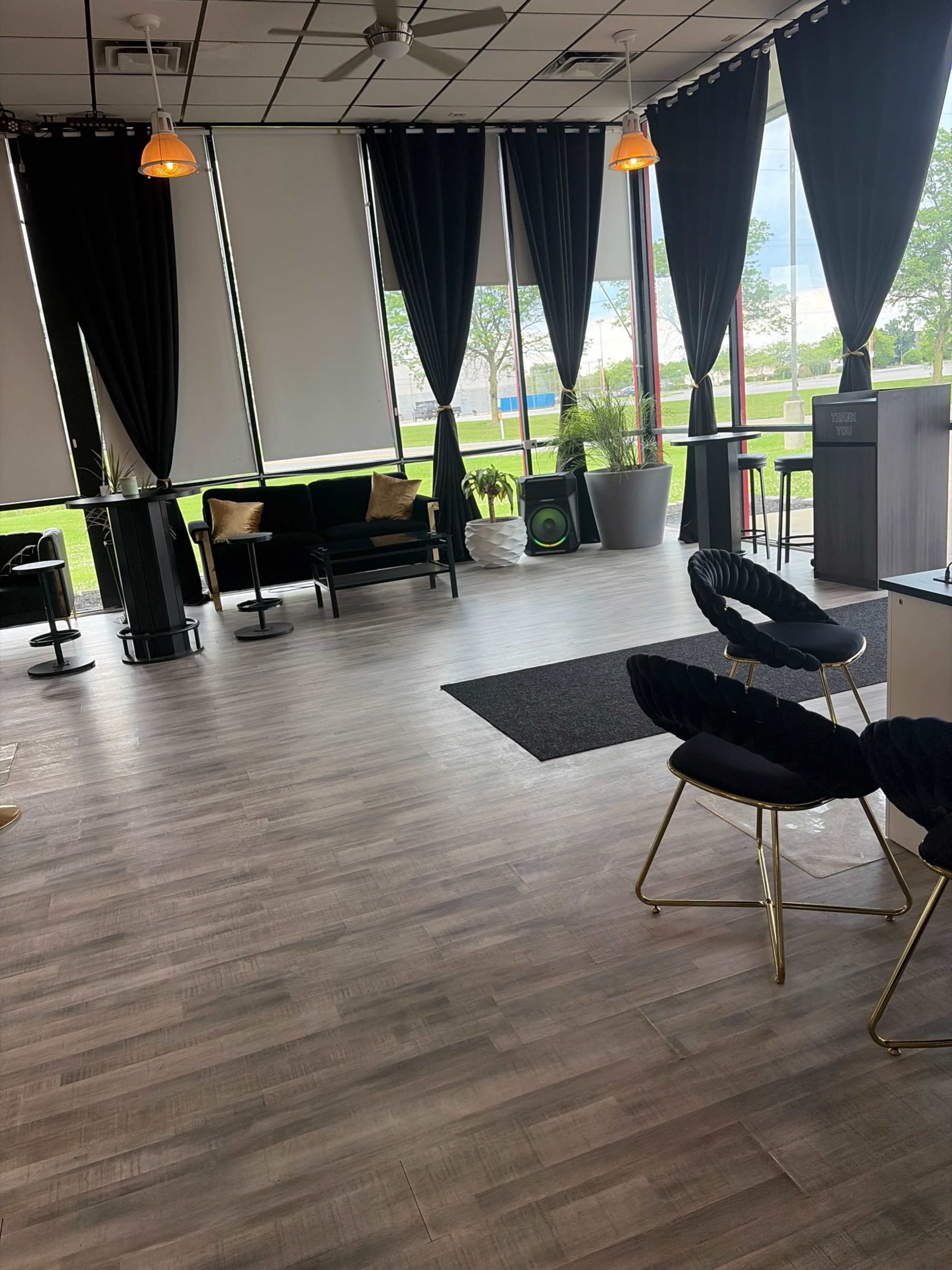 The image shows a modern interior space with large windows, dark curtains, and contemporary furniture arranged around a wooden floor.