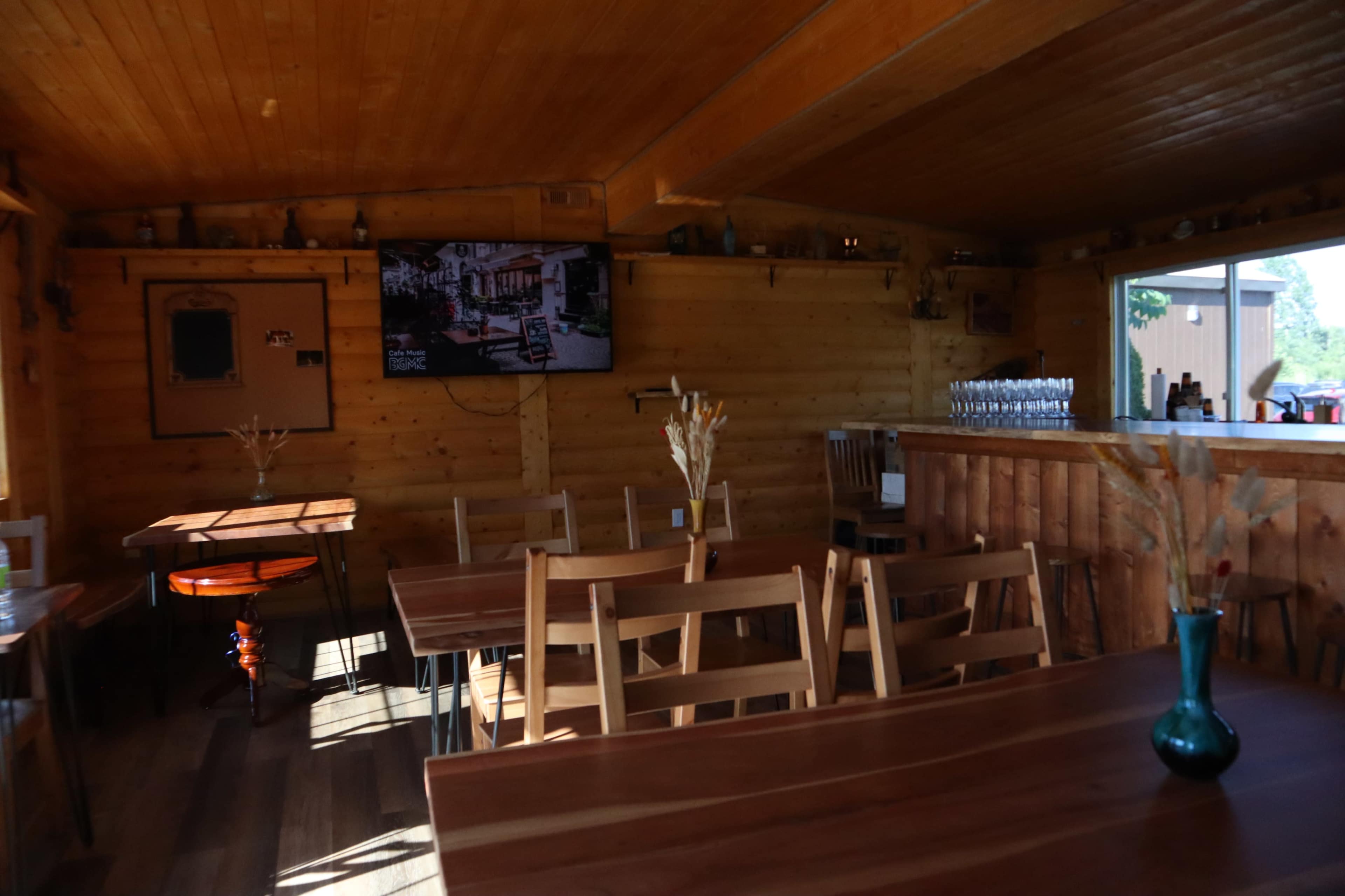 The image shows the interior of a wooden restaurant with tables, chairs, a bar, and a television mounted on the wall.