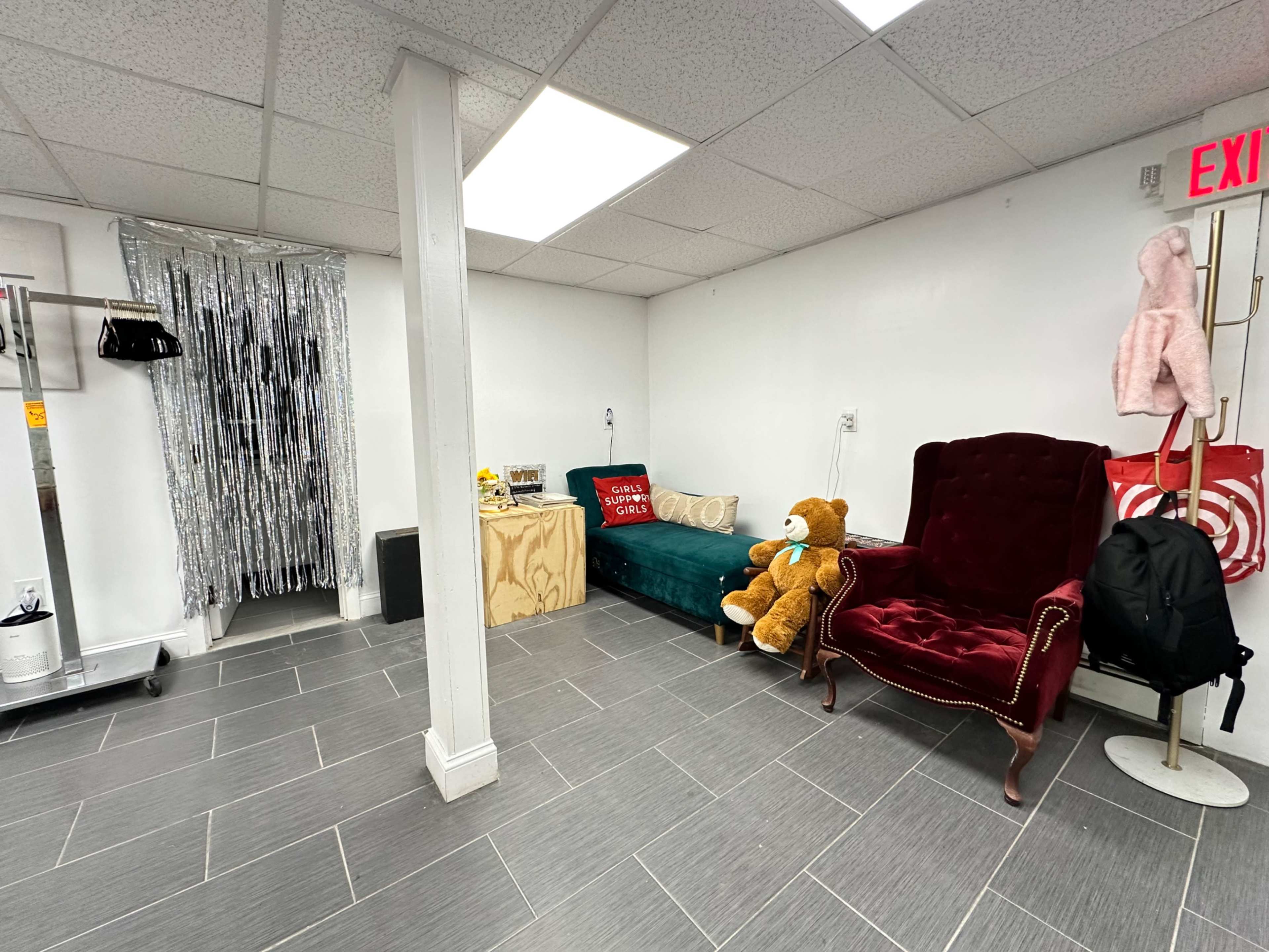 The image shows a small room with two chairs, a teddy bear, and a metallic curtain on one wall.