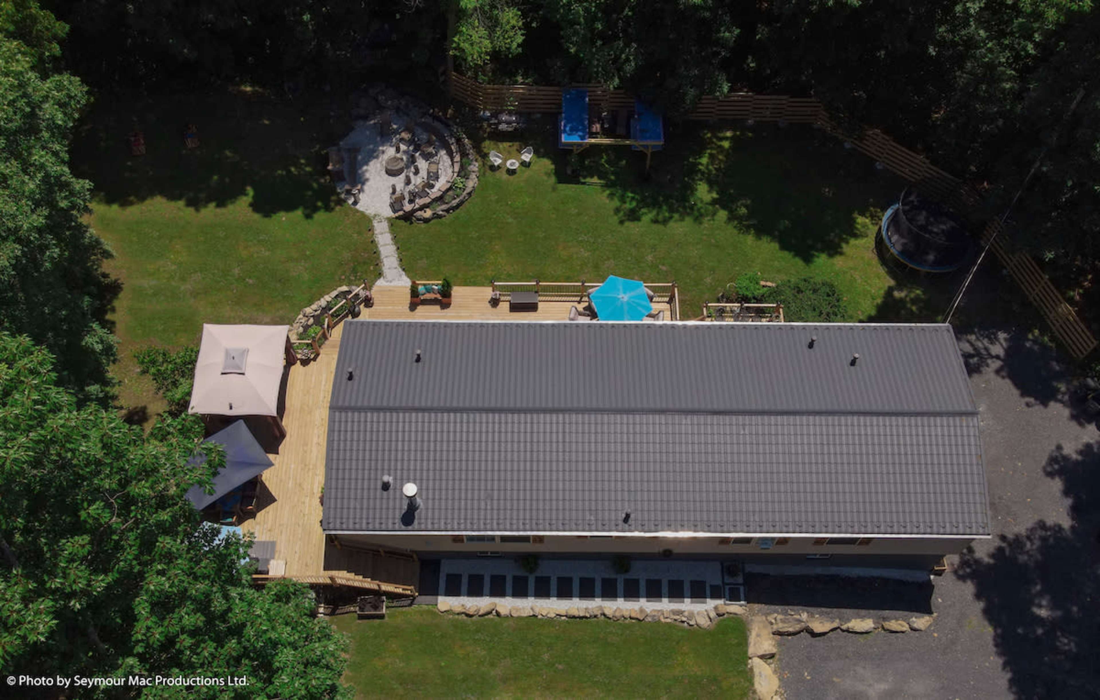 An aerial view of a large, rectangular building surrounded by landscaped grounds that include sitting areas, a stone fire pit, and a blue umbrella.