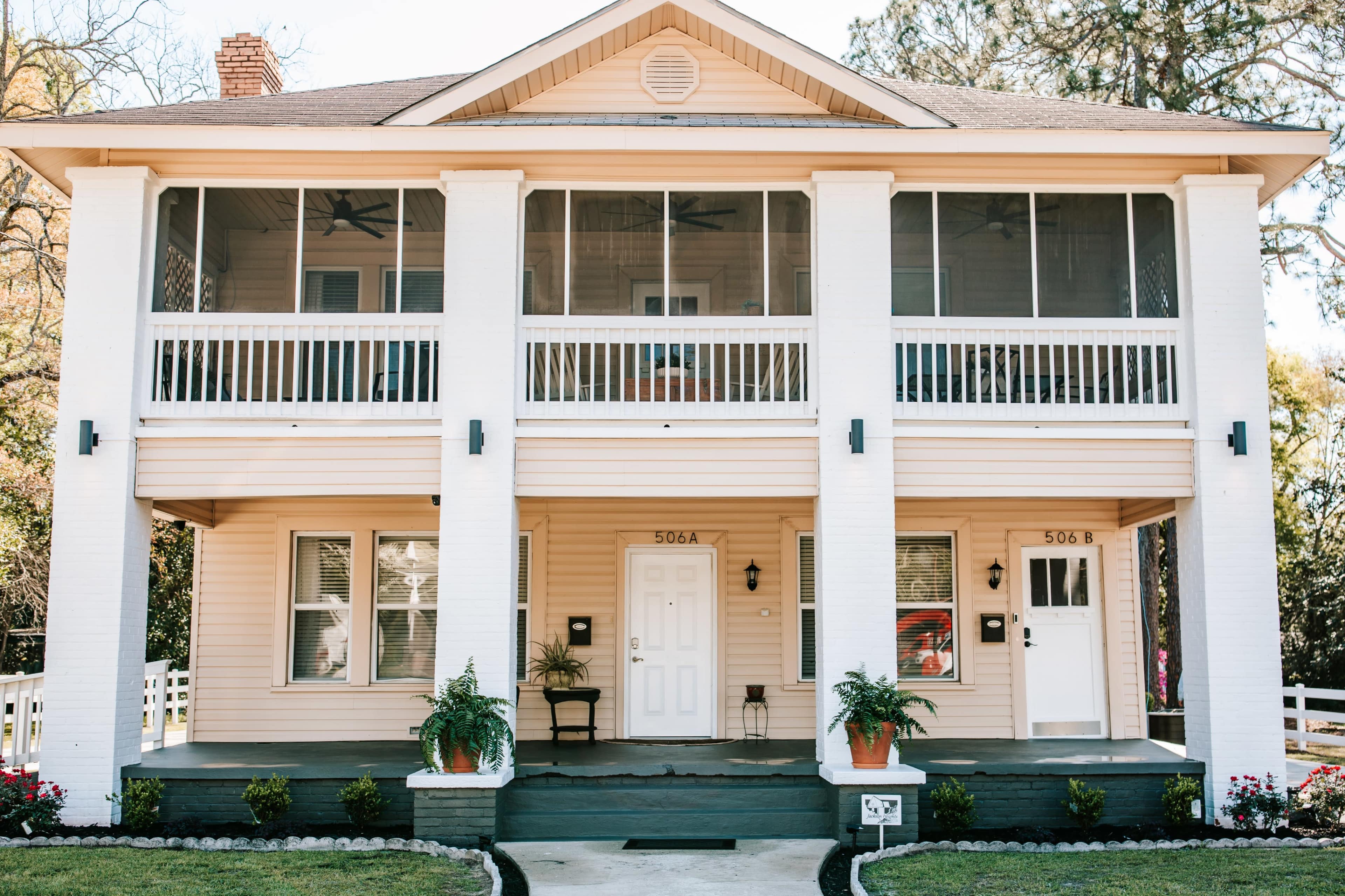 The image shows a two-story house with a screened-in porch, featuring two front doors labeled 506A and 506B, and surrounded by potted plants and a neatly maintained lawn.