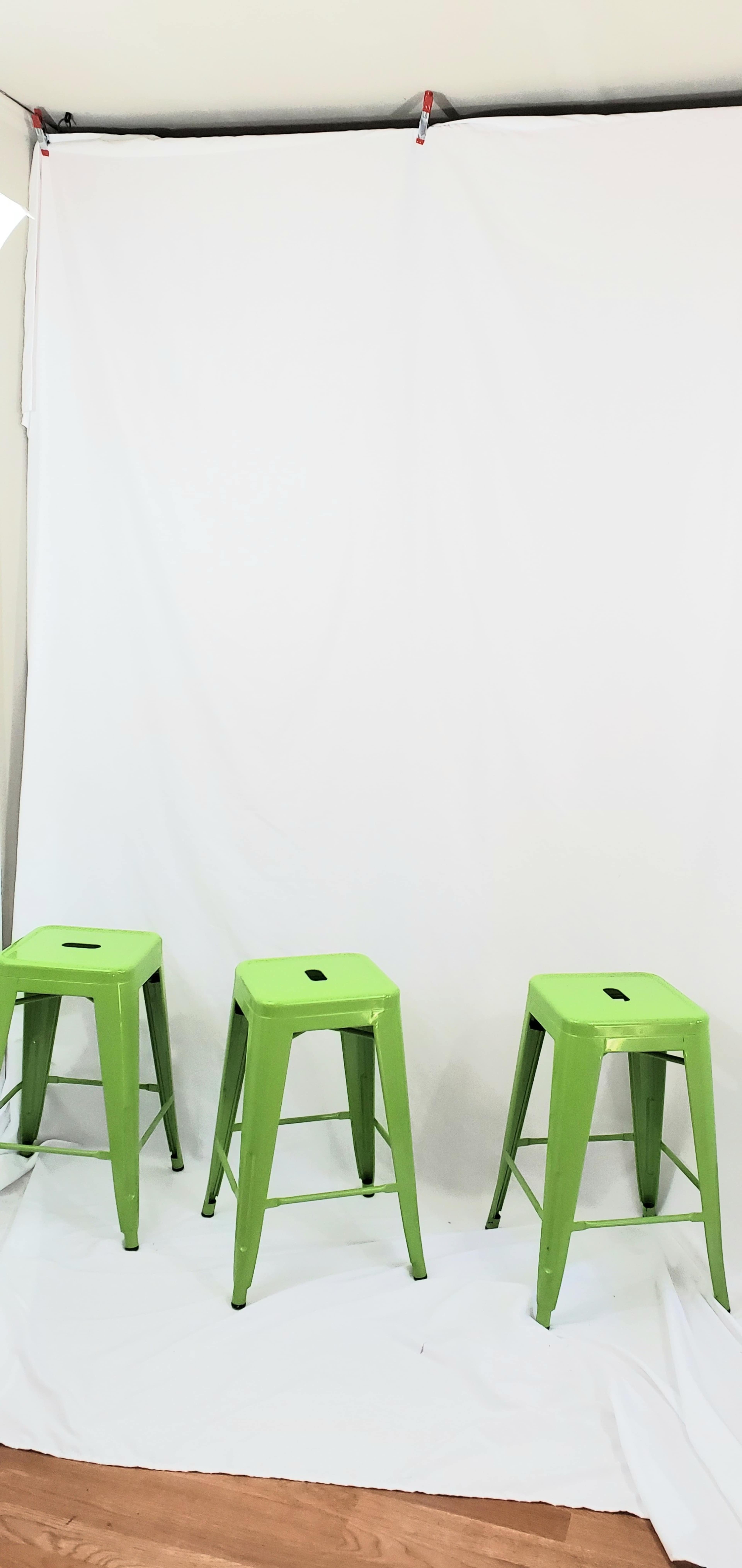 Three green metal stools are positioned in front of a white backdrop.