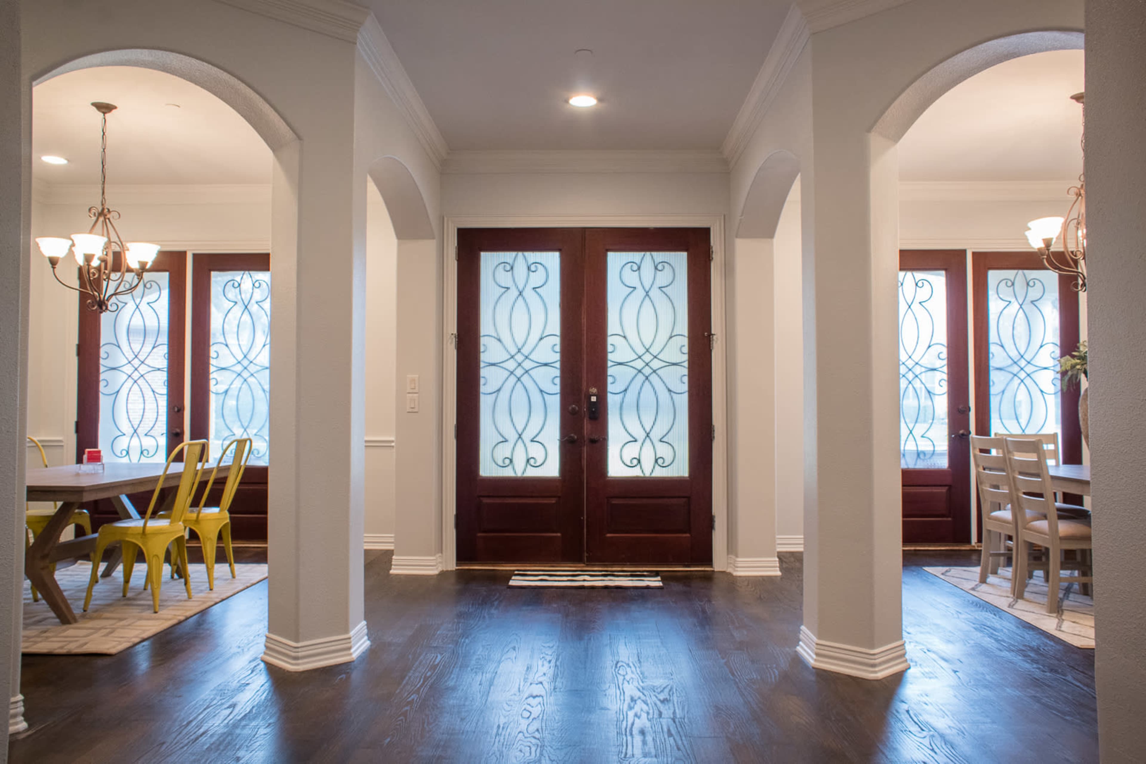 A hallway leading to two double doors with decorative glass, flanked by arched openings into dining areas on either side.