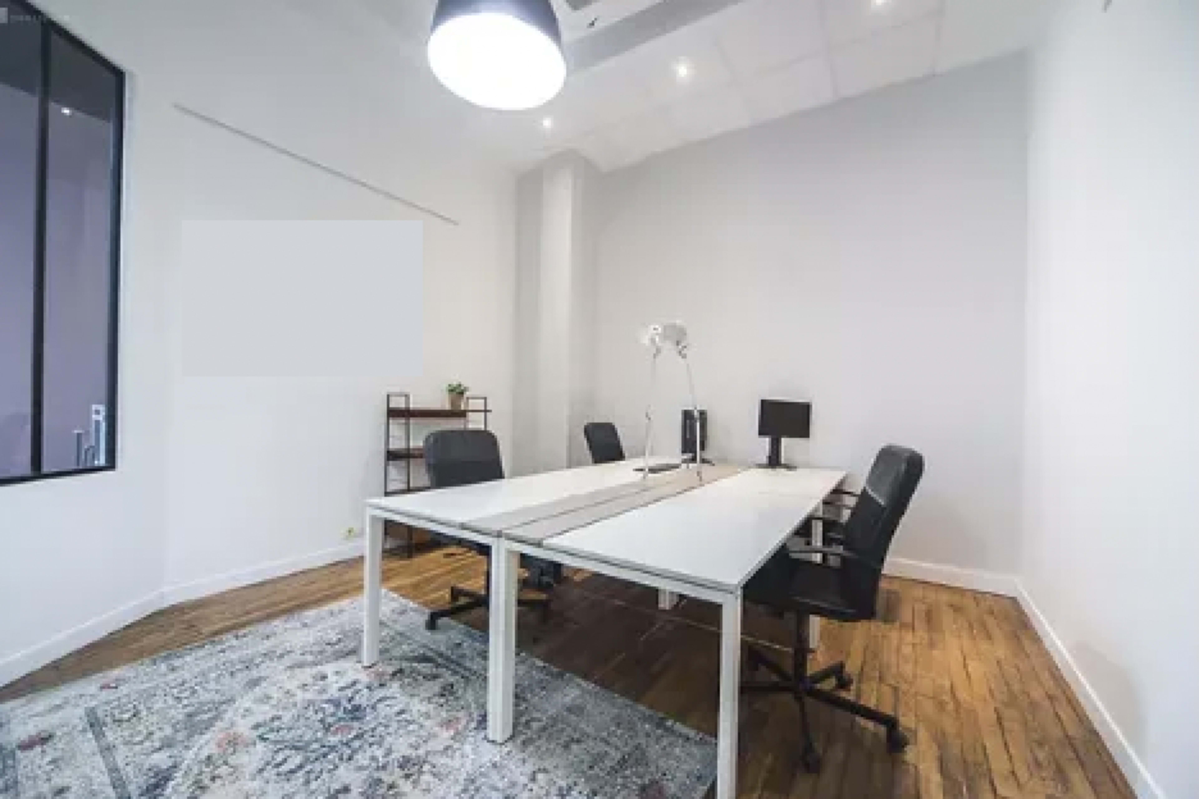 A modern office space with a large table, two chairs, a floor lamp, and a small shelf against the wall.