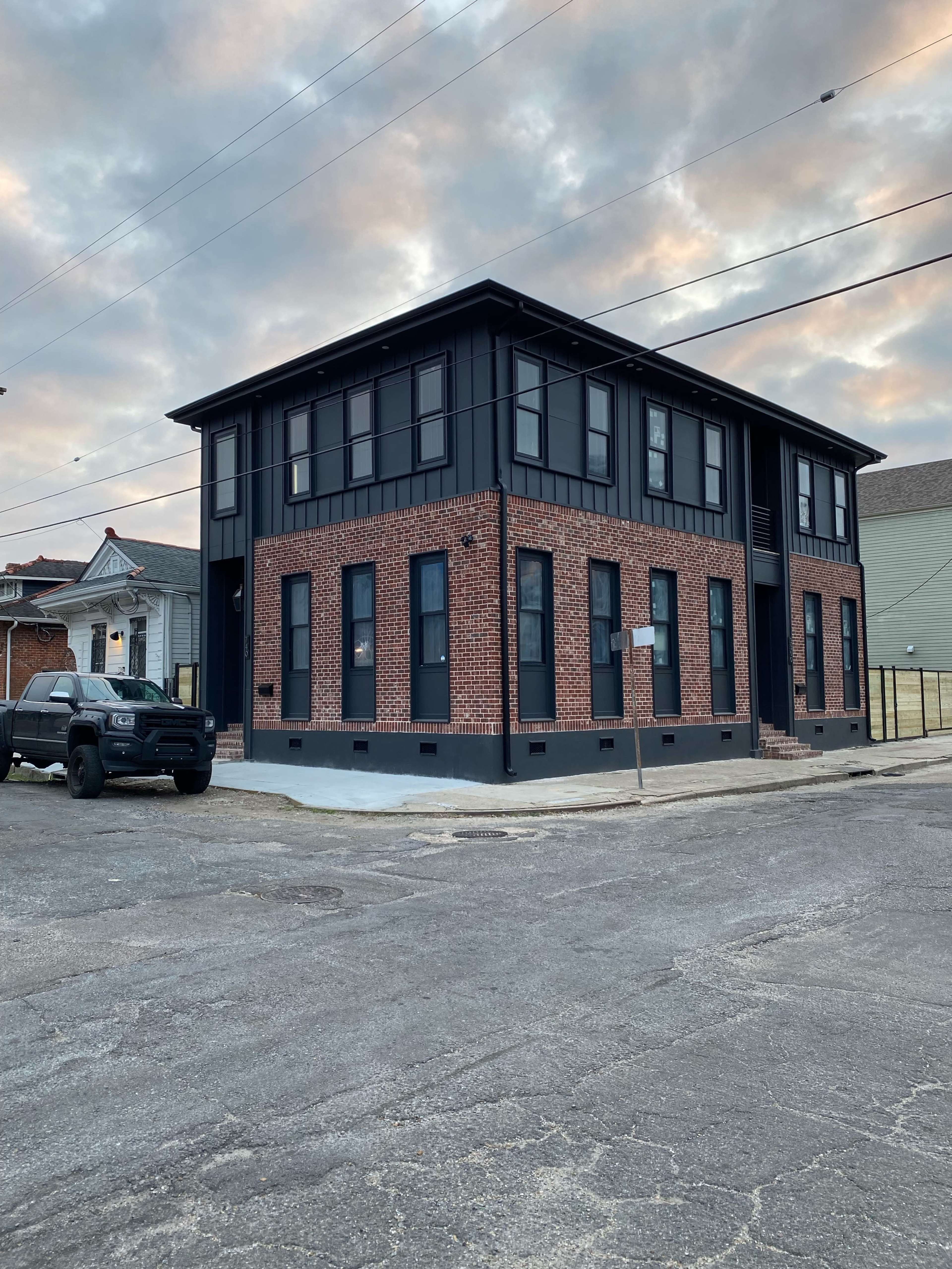 A two-story building with a brick exterior and large windows stands on a street corner, alongside a parked black pickup truck.