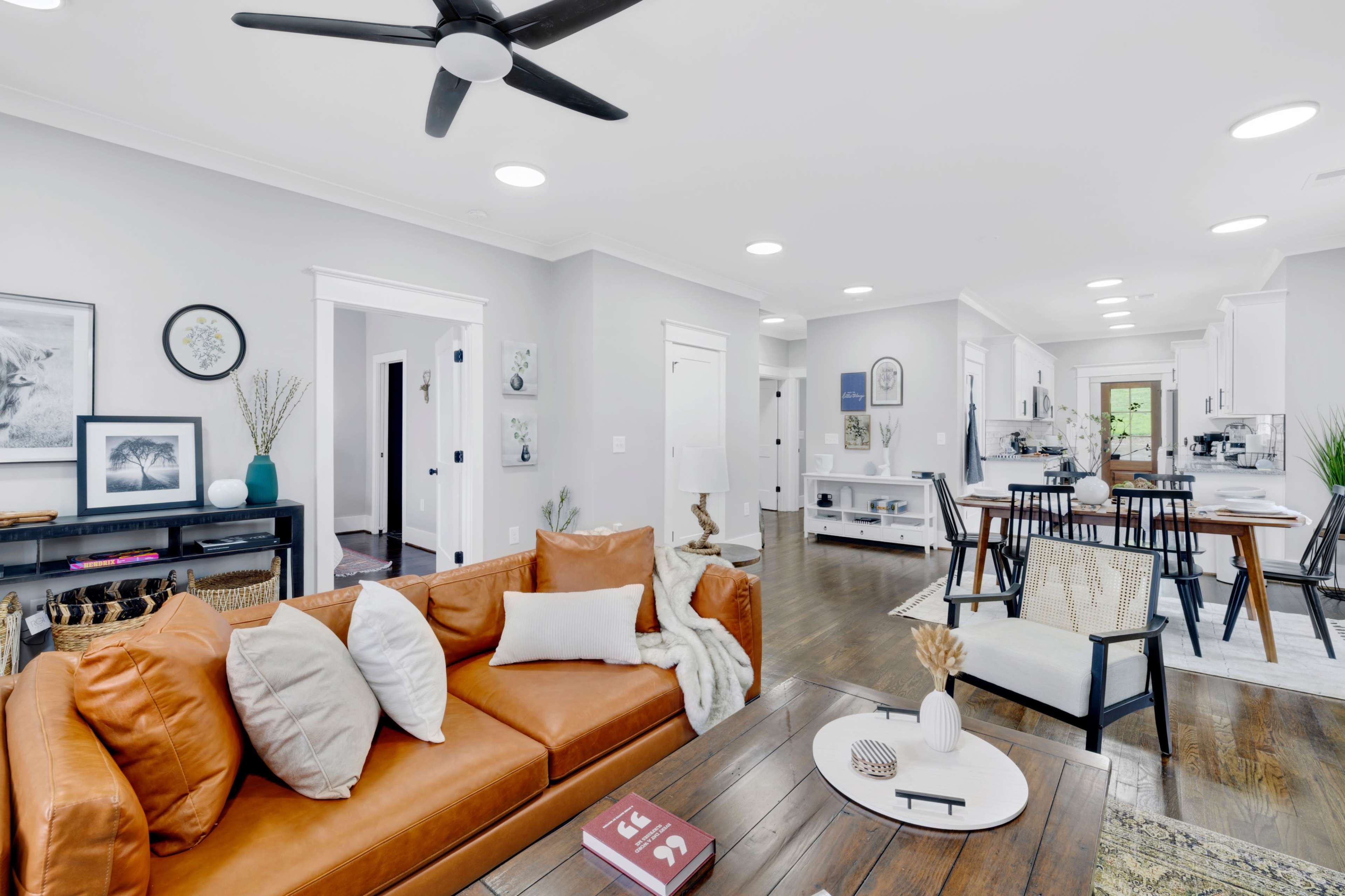 A modern living room with a brown leather sofa, a wooden coffee table, and a dining area visible in the background.