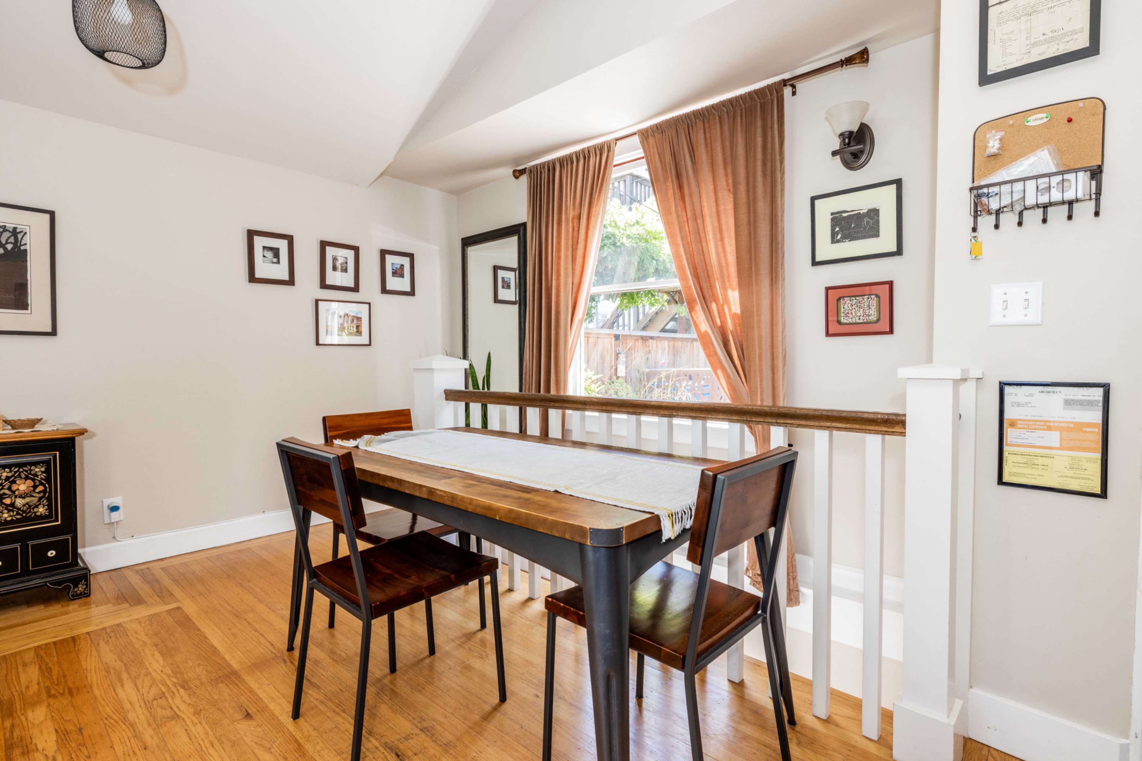 A small dining area features a table with four chairs, framed photographs on the walls, and a window with curtains.