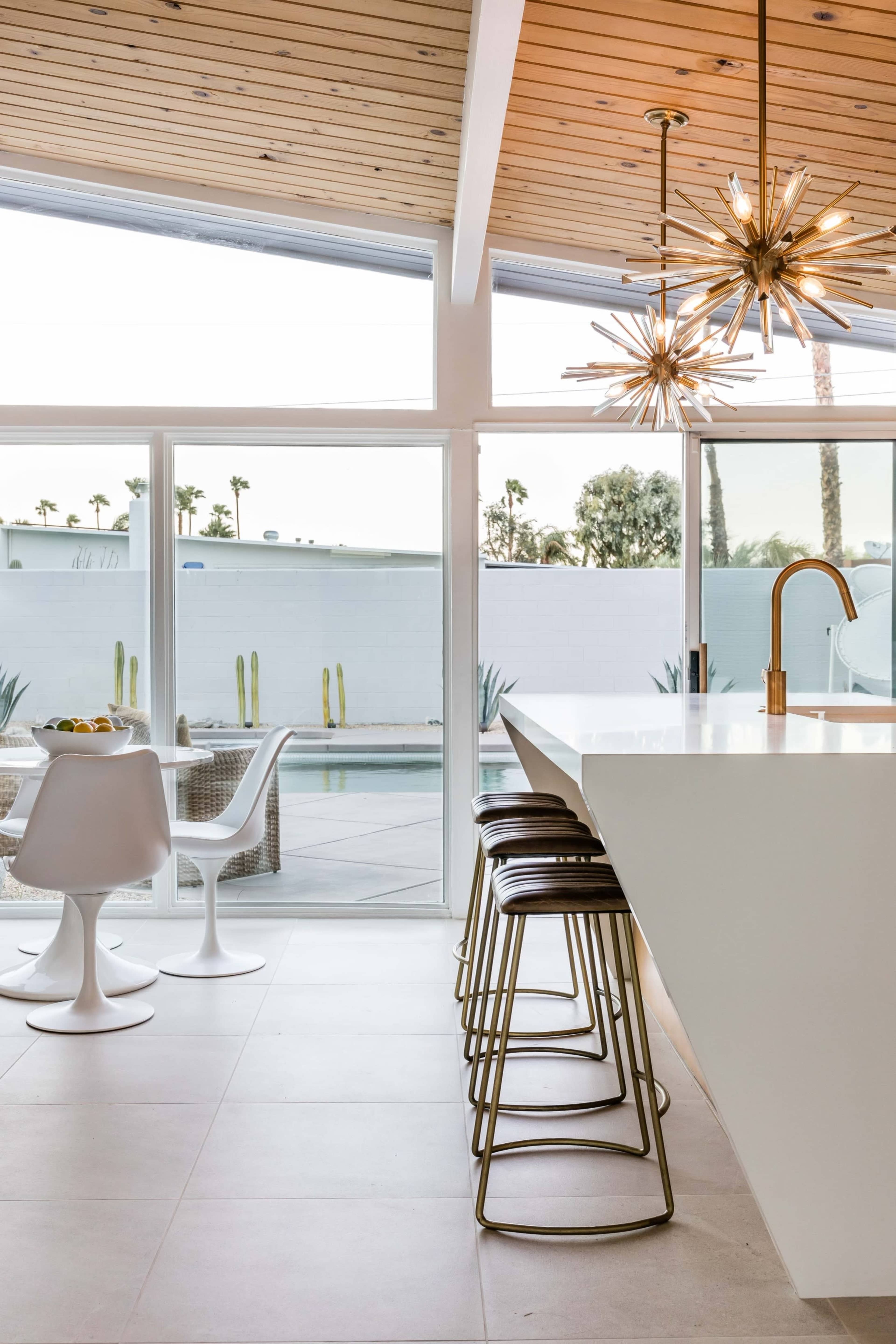 A modern kitchen with a large island, bar stools, and a view of a patio and pool area through large windows.