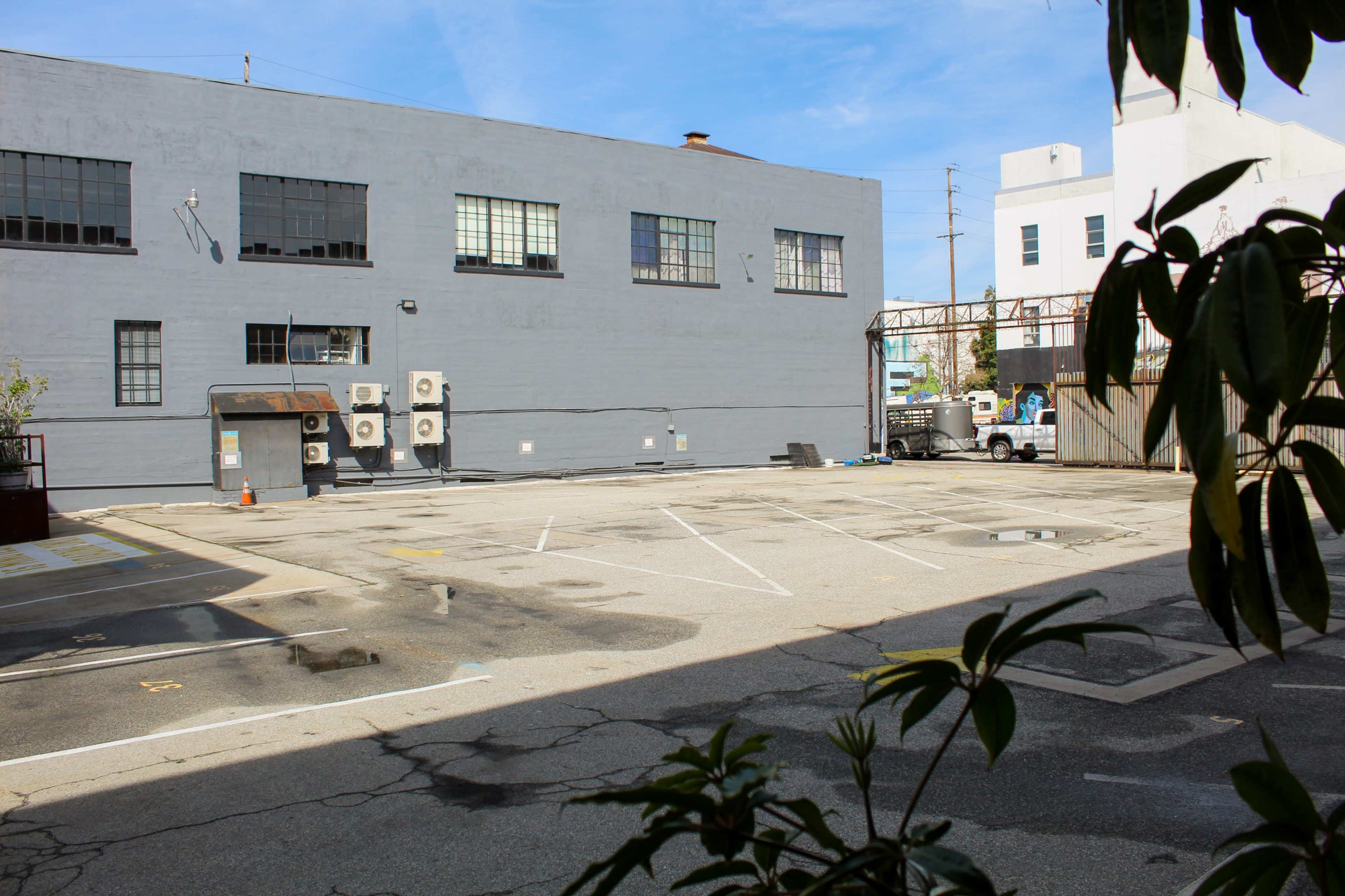 An empty parking lot with a gray building and air conditioning units in the background.