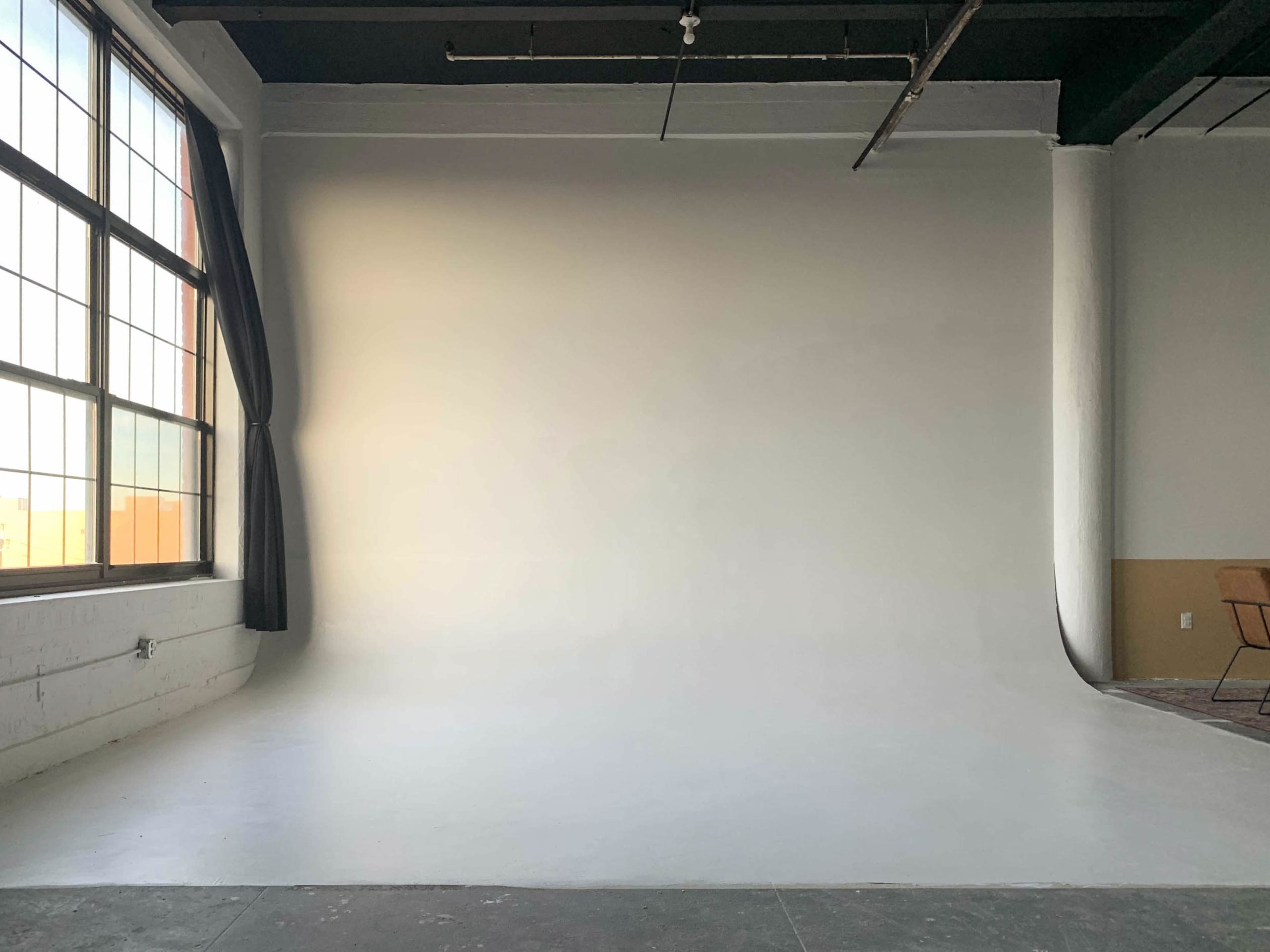 An empty photo studio with a large window and a seamless white backdrop.
