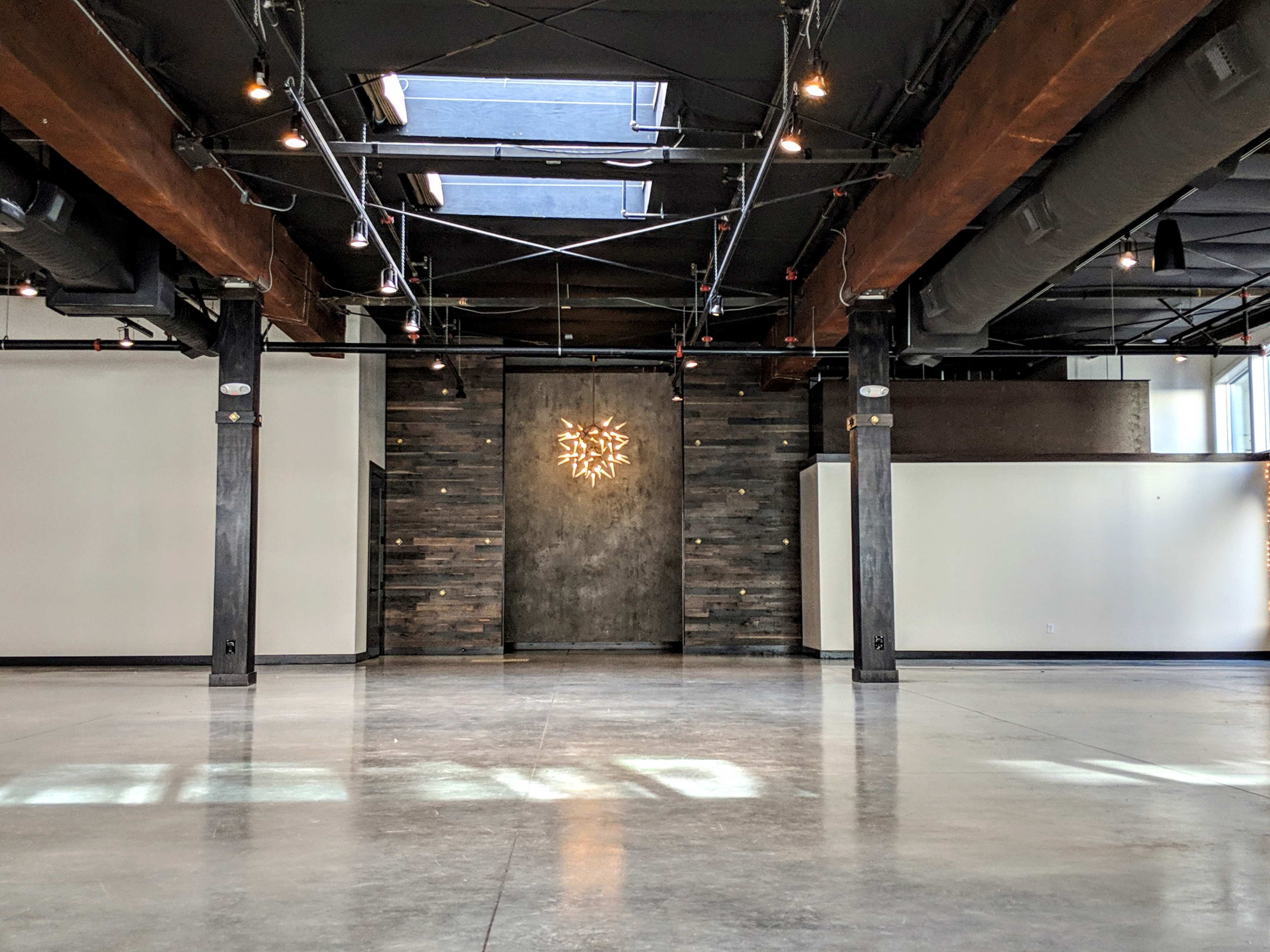 An expansive interior space with polished concrete floors, exposed wooden beams, and a wood-paneled feature wall illuminated by a decorative light fixture.