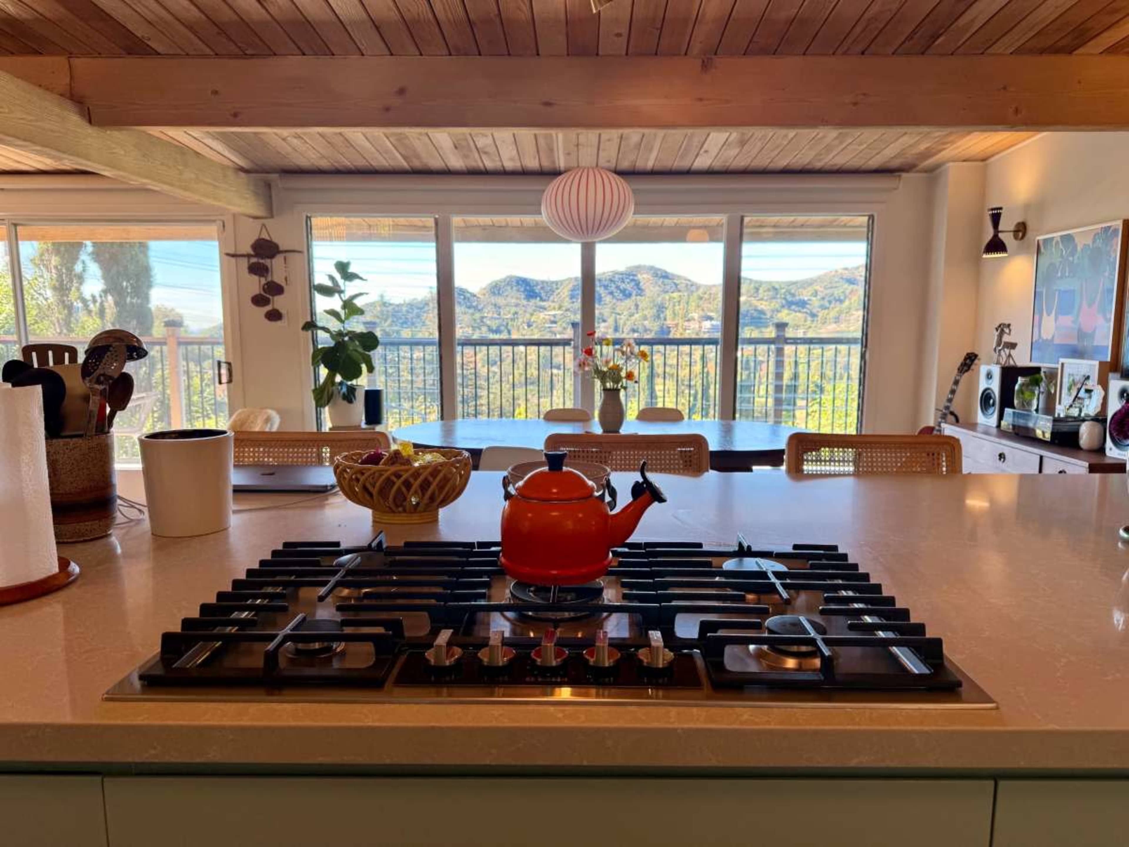 A modern kitchen with a red kettle on the stove and large windows showcasing a mountainous view beyond.