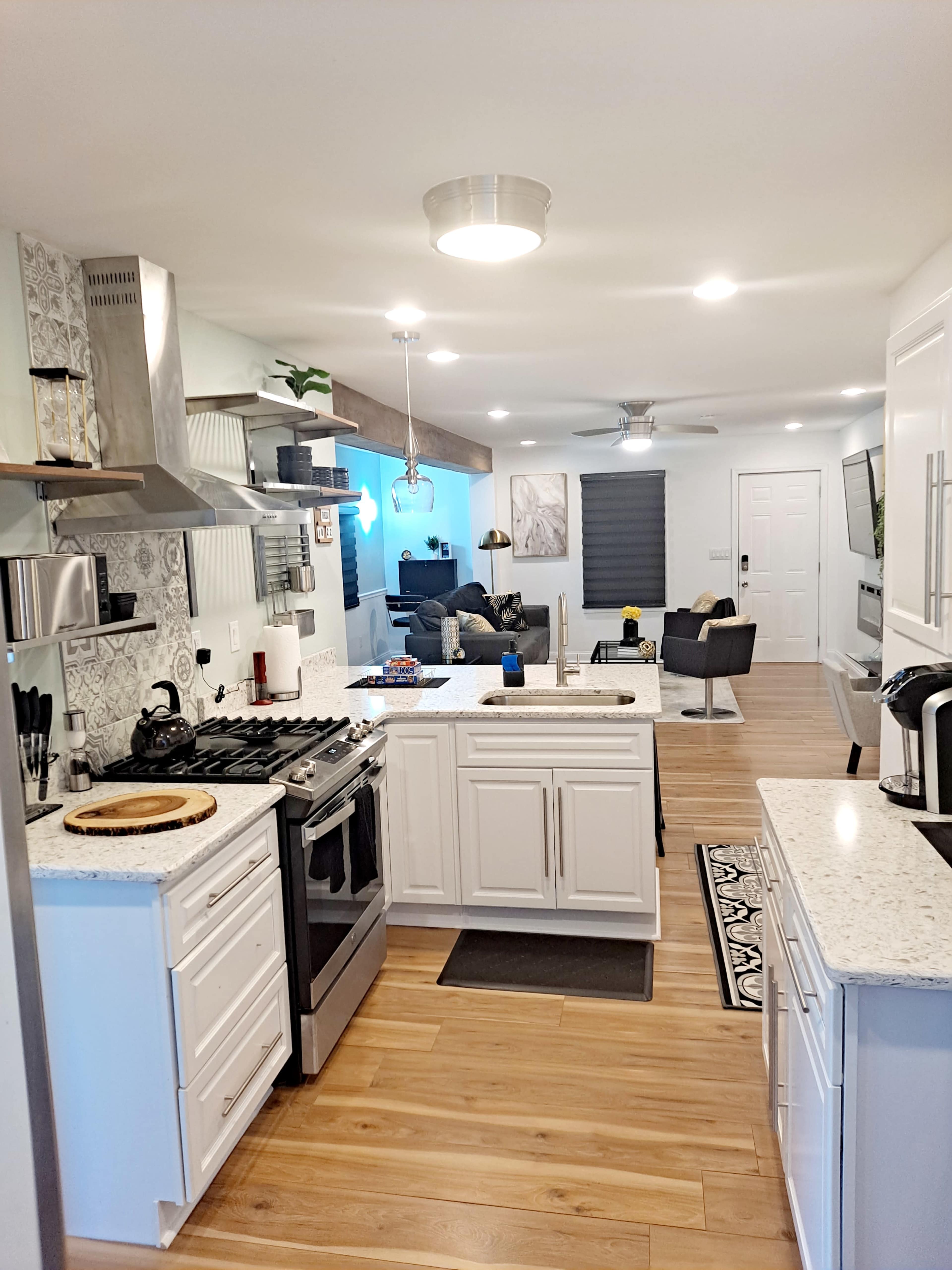 A modern kitchen with white cabinetry and a view into a living area featuring a sofa and flat-screen TV.