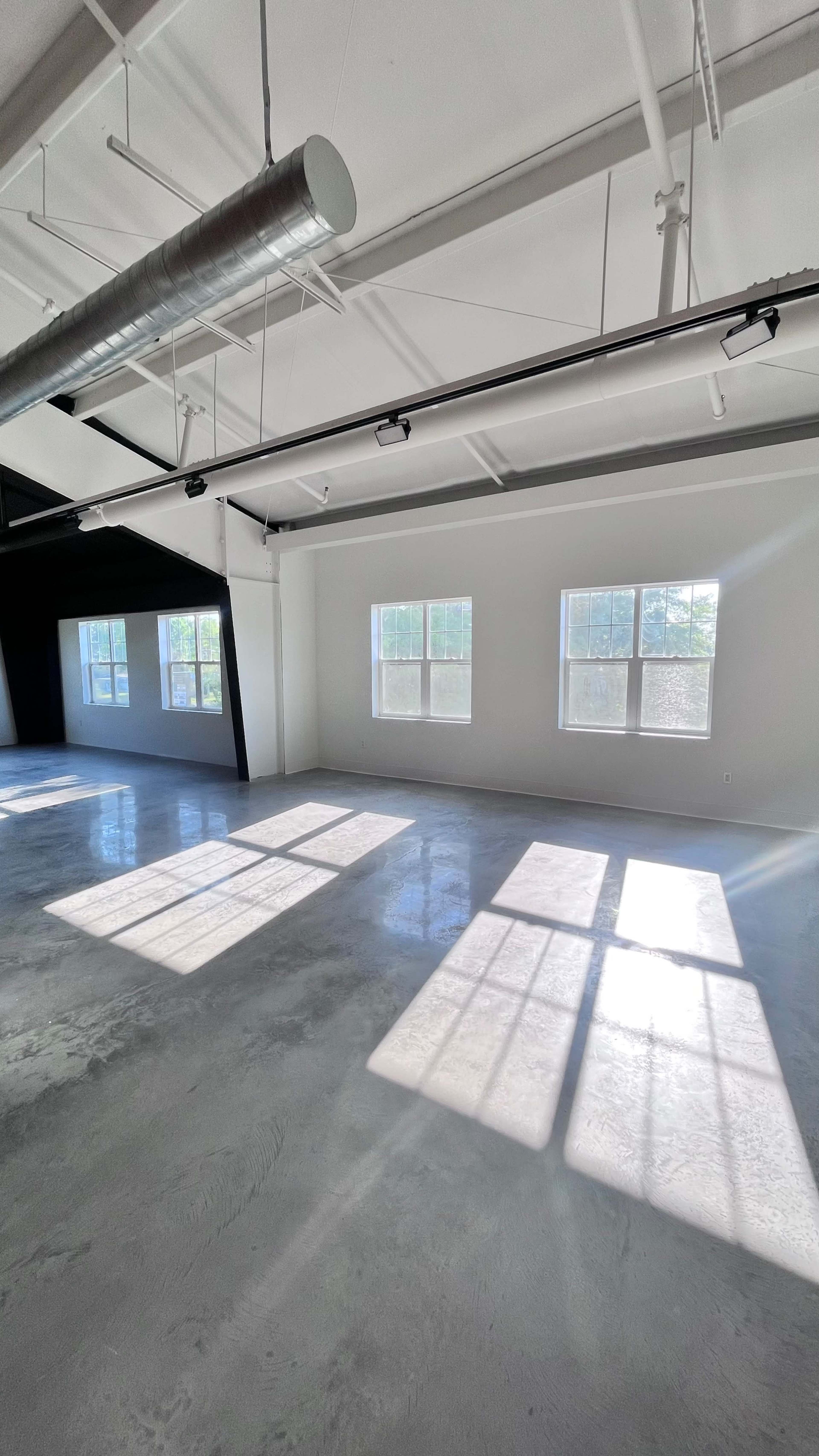 The image shows an empty room with polished concrete floors and large windows allowing sunlight to cast shadows on the surface.